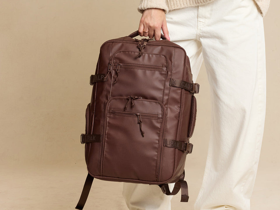 CALPAK Terra 35L Laptop Backpack in brown Walnut being held by a person on tan background