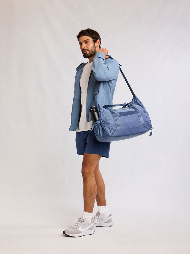 Man carrying on his shoulders the CALPAK Fit Duffel in blue Indigo