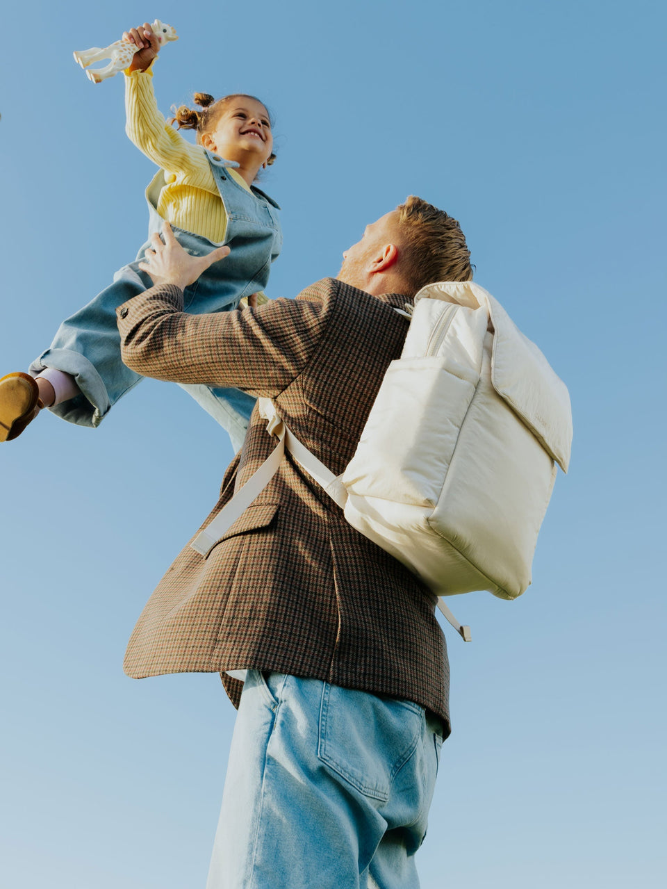 Dad carrying toddler in the air while wearing CALPAK Diaper Backpack with Laptop Sleeve in Oatmeal on his back