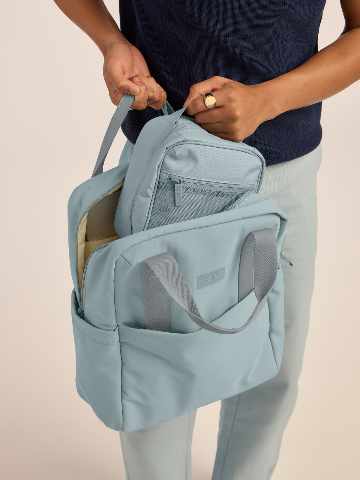 Model putting in the CALPAK Everything Cube in blue Bluebell in CALPAK Connect Backpack; ACE2401-BLUEBELL