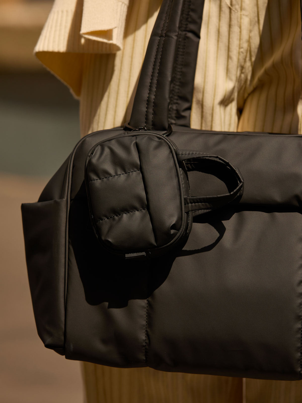 CALPAK Luka Duffel Key Pouch in pink Matte Black clipped onto the Luka Duffel in pink Matte Black being held by a model; ALK2501-MATTE-BLACK