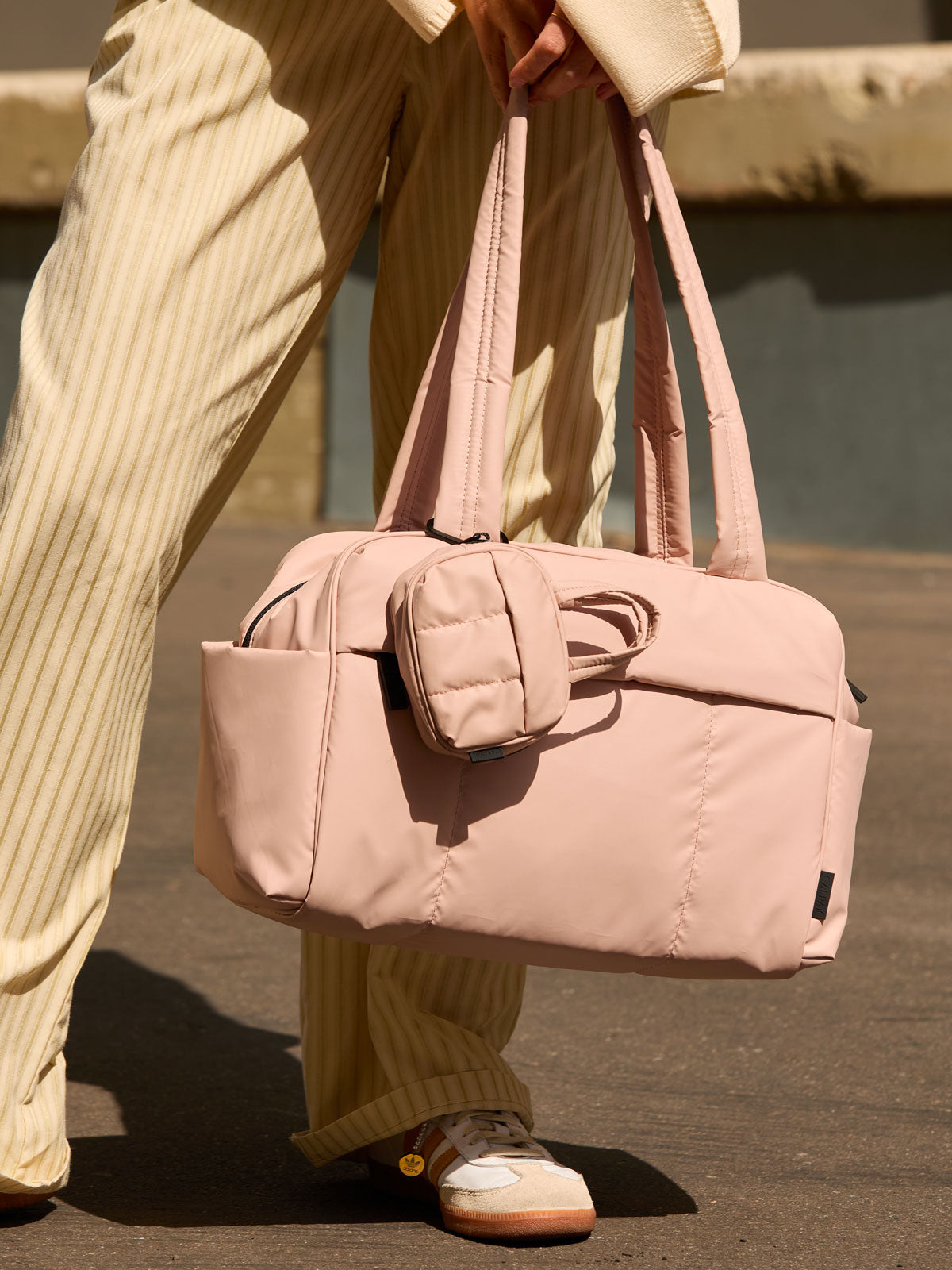 CALPAK Luka Duffel Key Pouch in pink Rose Quartz clipped onto the Luka Duffel in pink Rose Quartz being held by a model; ALK2501-ROSE-QUARTZ