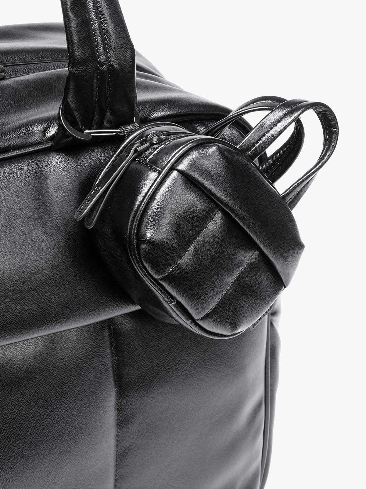 A close-up of a Black vegan leather top-handle CALPAK Luka Zip Bag Charm with a zippered front pocket and a small side strap  with a matching small zippered pouch attached near the handle, shown against a clean white background;  ALK2501-BLACK-PU