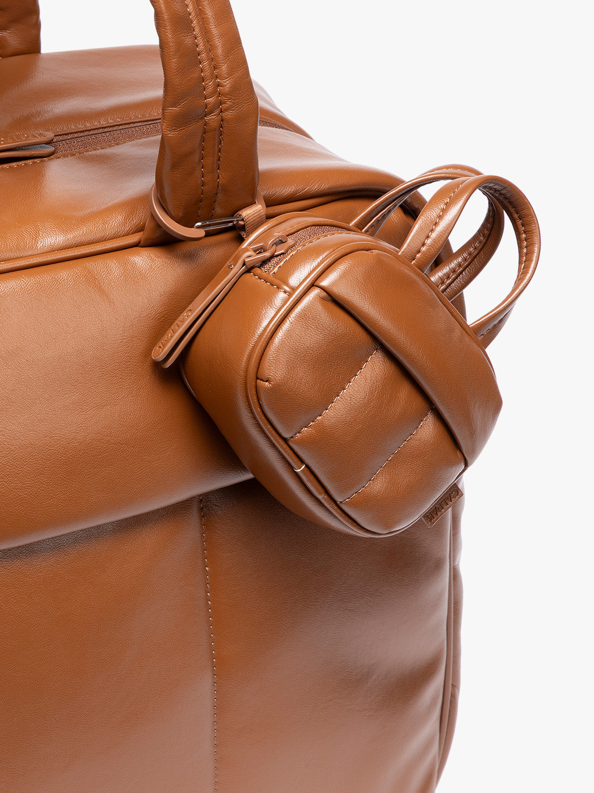 A close-up of a light Honey Brown vegan leather top-handle CALPAK Luka Zip Bag Charm with a zippered front pocket and a small side strap  with a matching small zippered pouch attached near the handle, shown against a clean white background; ALK2501-HONEY-BROWN-PU