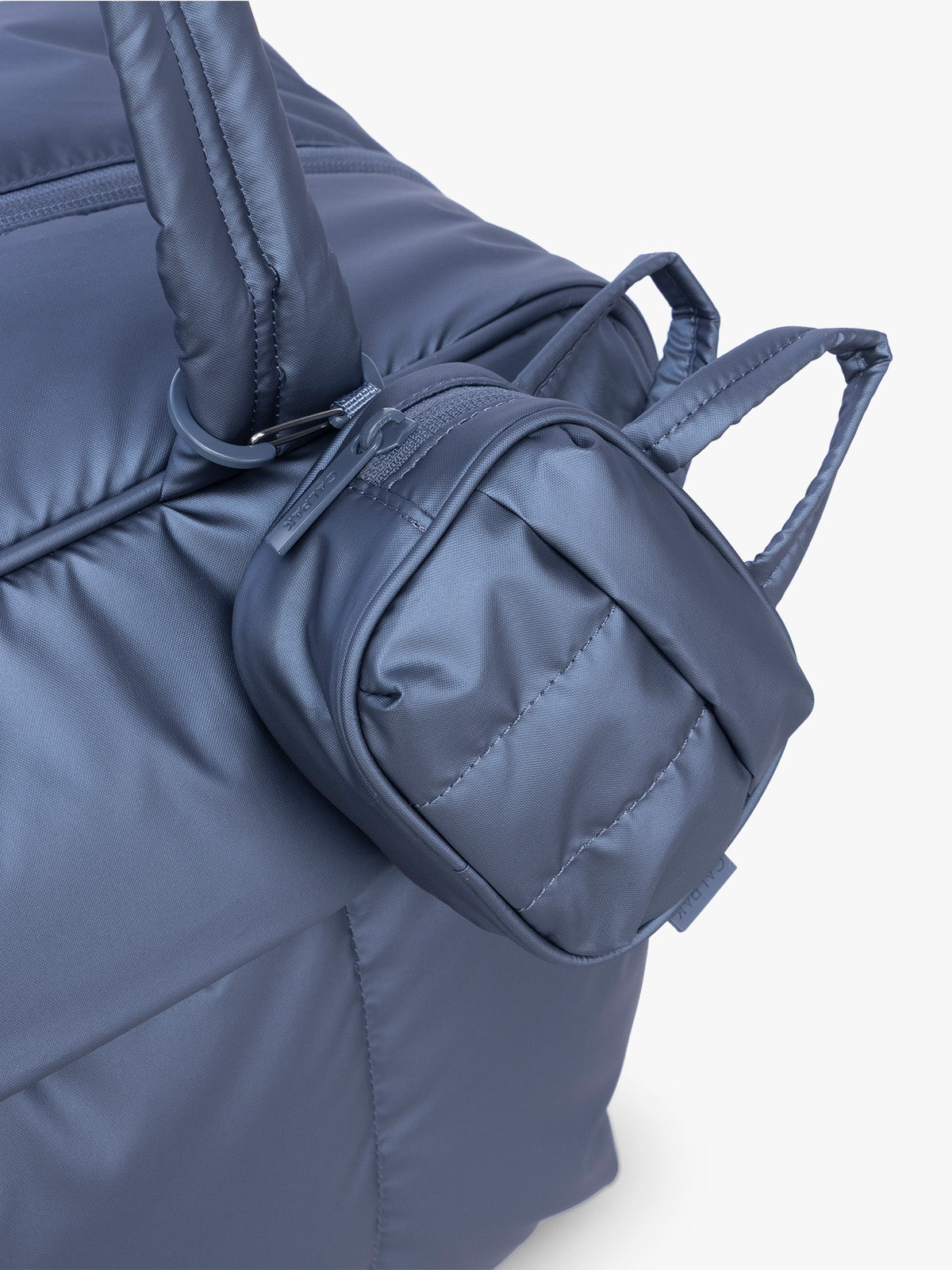 CALPAK Luka Duffel Zip Bag Charm in dark blue metallic material in Metallic Indigo clipped on a bag; ALK2501-METALLIC-INDIGO