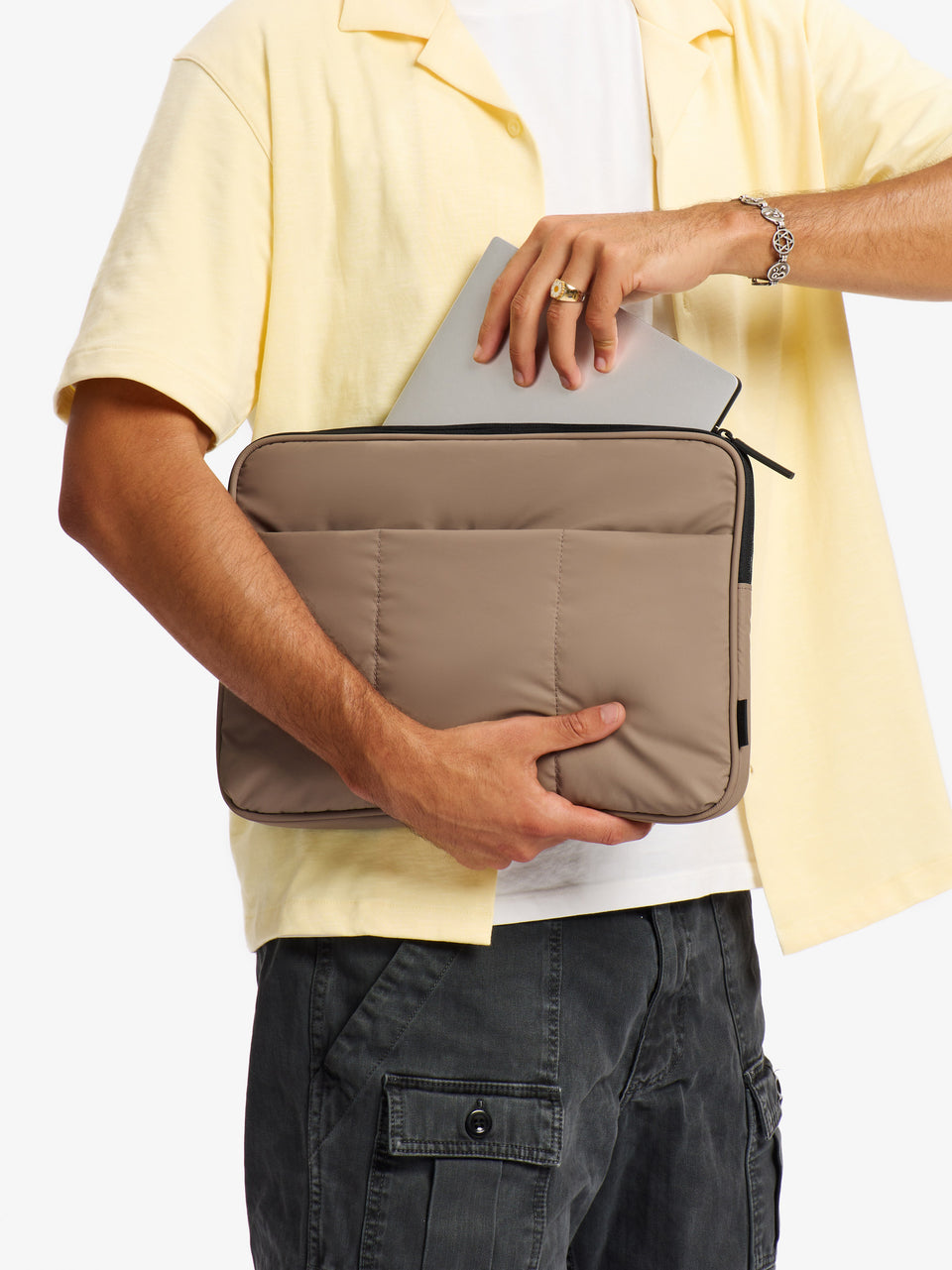 Model placing 14 inch laptop into main pocket of CALPAK Luka 14" Padded Laptop Sleeve in chocolate brown; ALL2401-CHOCOLATE