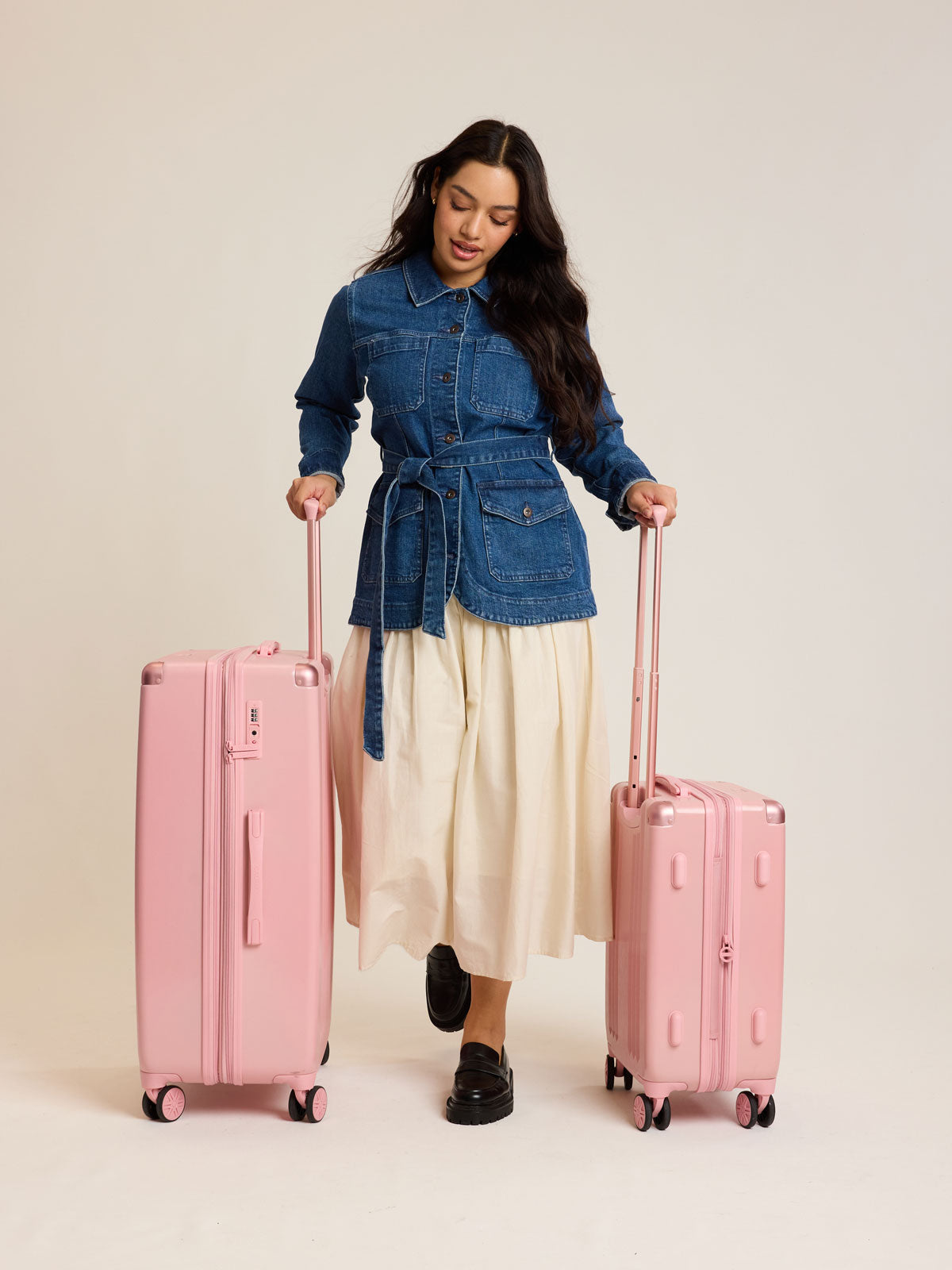 Model with CALPAK 2pc Ambeur Luggage Set featuring the Ambeur Carry-On Luggage and Ambeur Large Luggage in metallic pink Blossom with pink wheels;  LAM2000-BLOSSOM