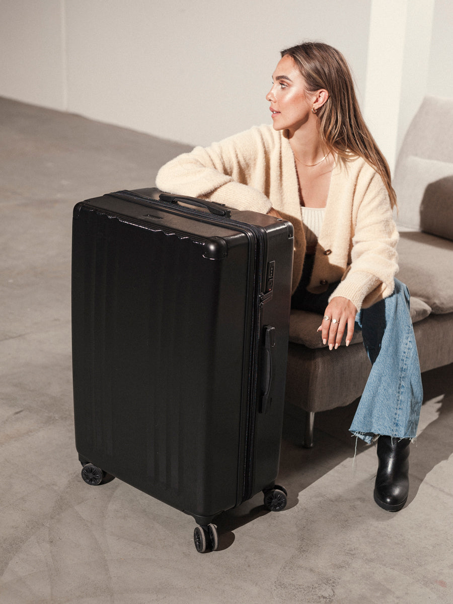 woman with large black CALPAK Ambeur hard shell spinner luggage; LAM1028-BLACK;