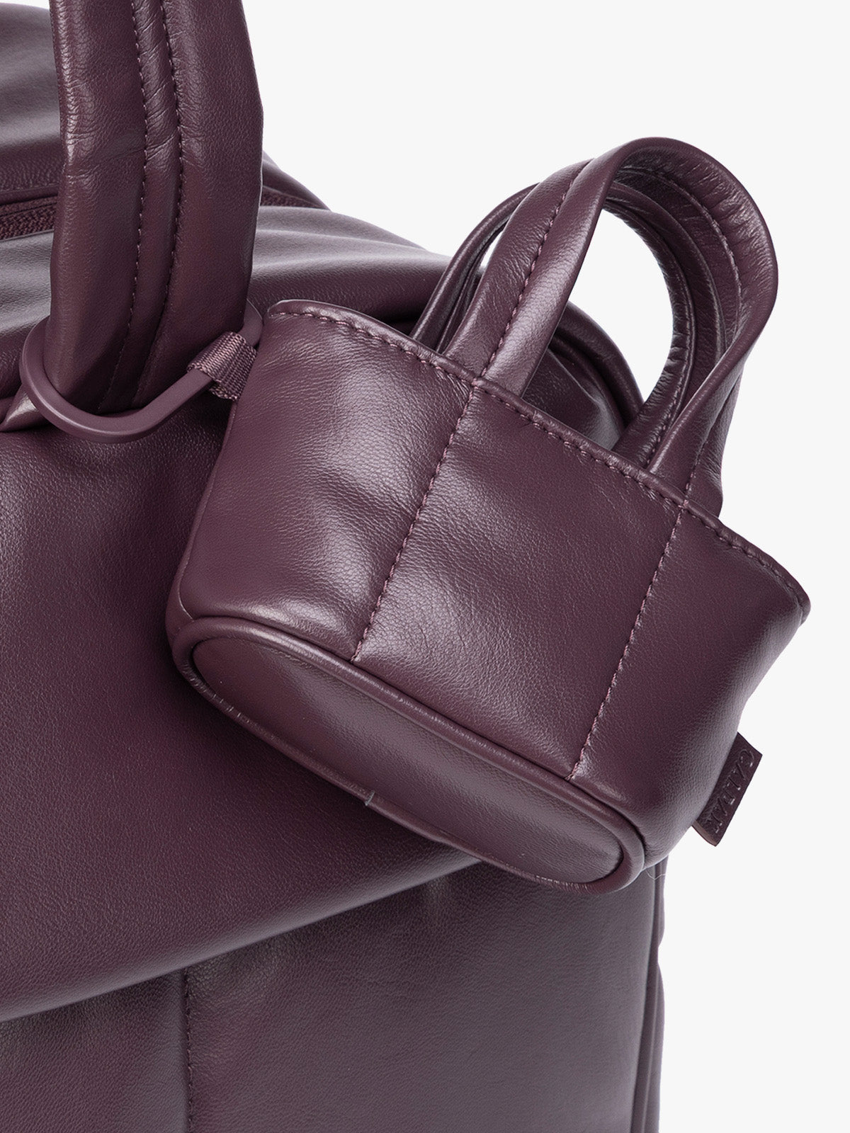 Closeup of A small deep burgundy Dark Cherry CALPAK Luka Tote Bag Charm with dual top handles and a black carabiner clip attached to the side, shown against a plain white background; AMT2601-DARK-CHERRY-PU