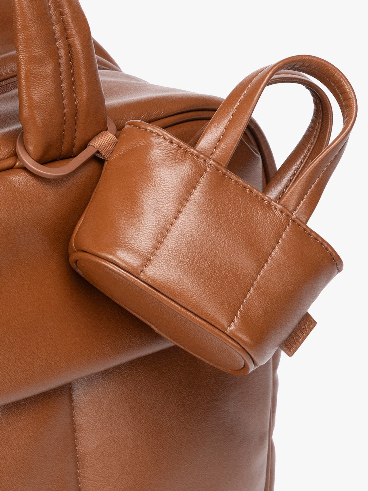 Closeup of a small light brown Honey Brown CALPAK Luka Tote Bag Charm with dual top handles and a black carabiner clip attached to the side, shown against a plain white background; AMT2601-HONEY-BROWN-PU