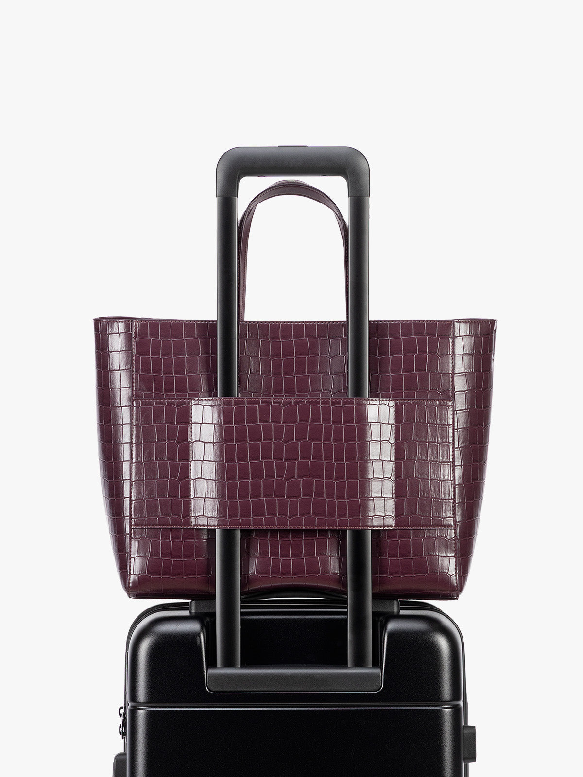 Backside luggage trolley sleeve of CALPAK Haven 15" Laptop Tote in deep red Dark Cherry crocodile-embossed with dual top handles and a matching shoulder strap against a plain white background; ATS2501-DARK-CHERRY-FAUX-CROC