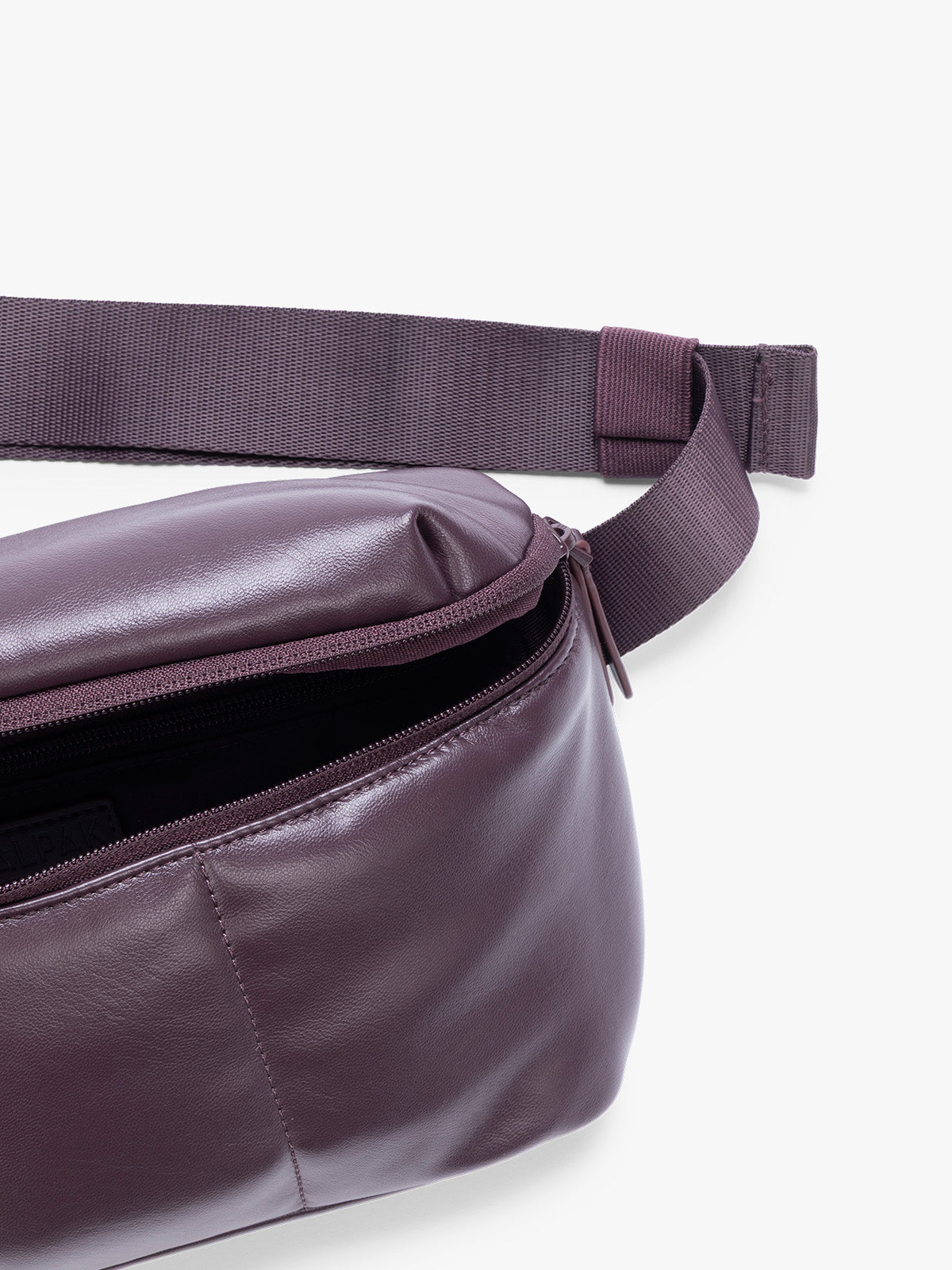 Closeup of front zipper pocket with crossbody strap of a deep burgundy Dark Cherry vegan leather CALPAK Luka Belt Bag with a zippered front pocket and side straps, shown against a plain white background; BB1901-DARK-CHERRY-PU
