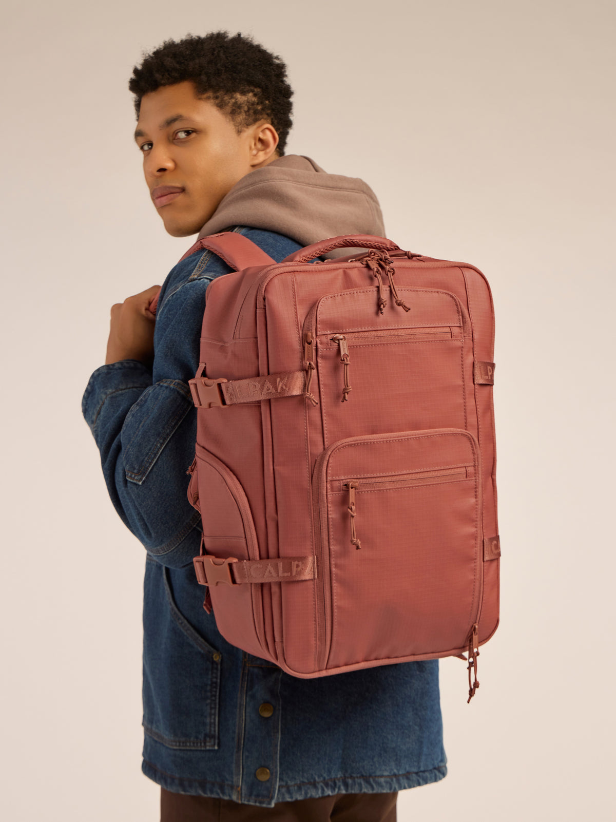 Model wearing the CALPAK Terra 26L Laptop Backpack Duffel in red and orange Matte Clay; BPH2201-CLAY