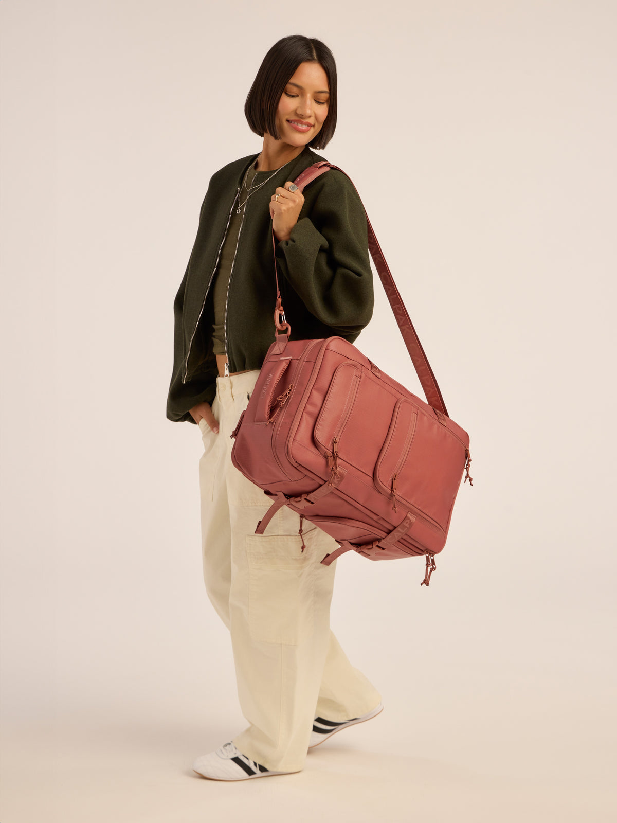 Model wearing CALPAK Terra 26L Laptop Backpack Duffel in red and orange Matte Clay duffel; BPH2201-CLAY