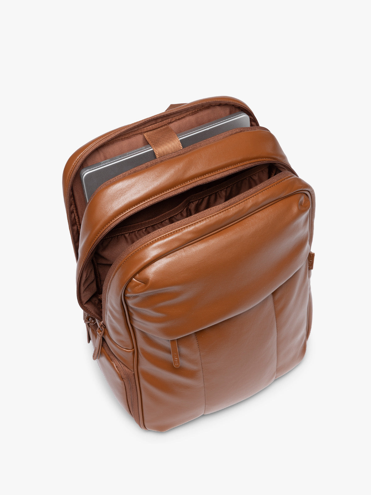 Laptop sleeve of CALPAK Honey Brown Luka 15 inch Laptop Backpack in vegan leather with a glossy finish, featuring a top carry handle, a main zippered compartment, and a front slip pocket, shown against a plain white background; BPL2001-HONEY-BROWN-PU
