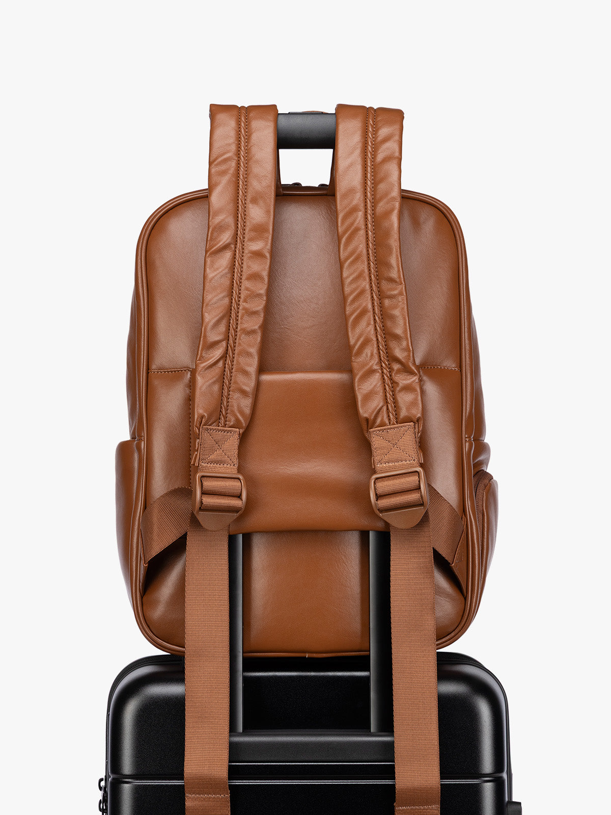 Backside luggage trolley sleeve of CALPAK Honey Brown Luka 15 inch Laptop Backpack in vegan leather with a glossy finish, featuring a top carry handle, a main zippered compartment, and a front slip pocket, shown against a plain white background; BPL2001-HONEY-BROWN-PU
