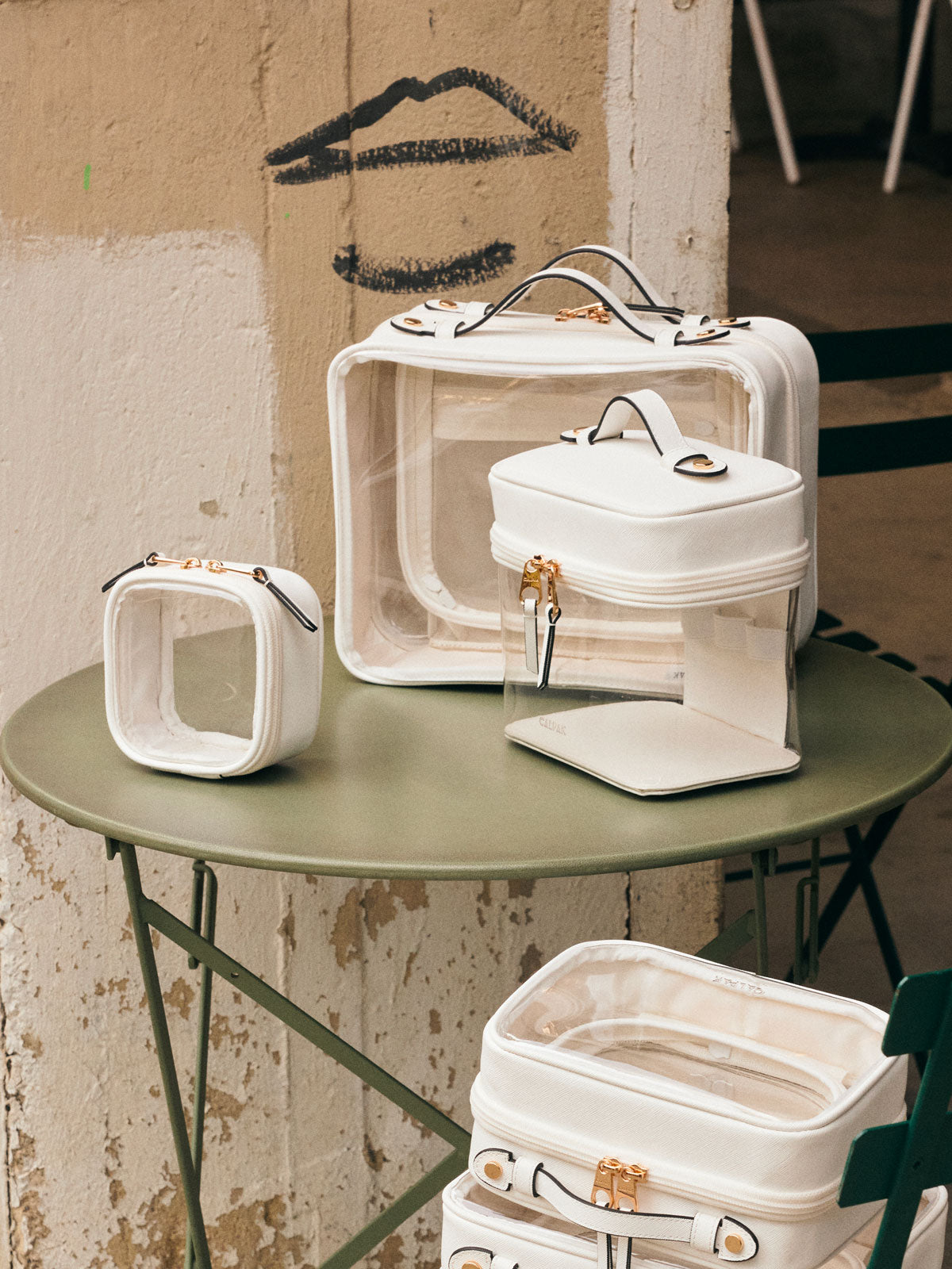 CALPAK Clear Train Case in White on a green table, with other CALPAK Clear Cosmetic Cases in white; CTC2401-WHITE