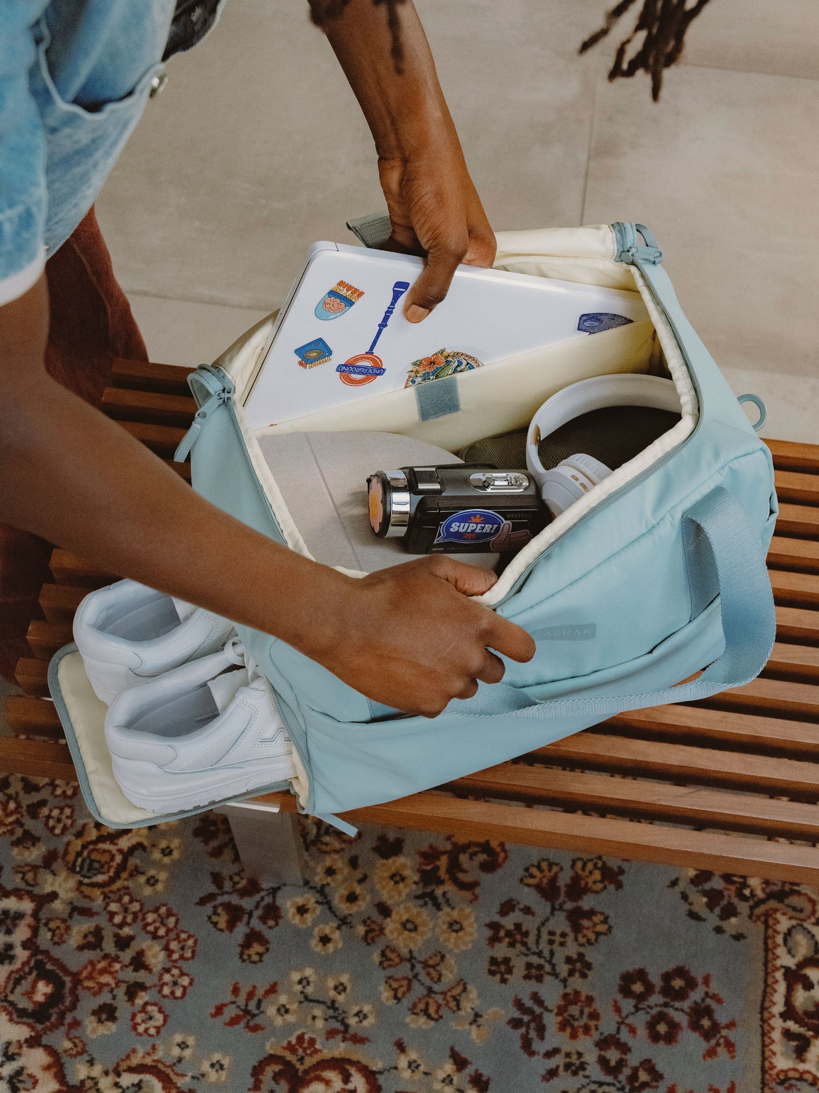 Model placing laptop within padded laptop sleeve of blue CALPAK Connect Laptop Duffel with other belongings inside; DCN2401-BLUEBELL