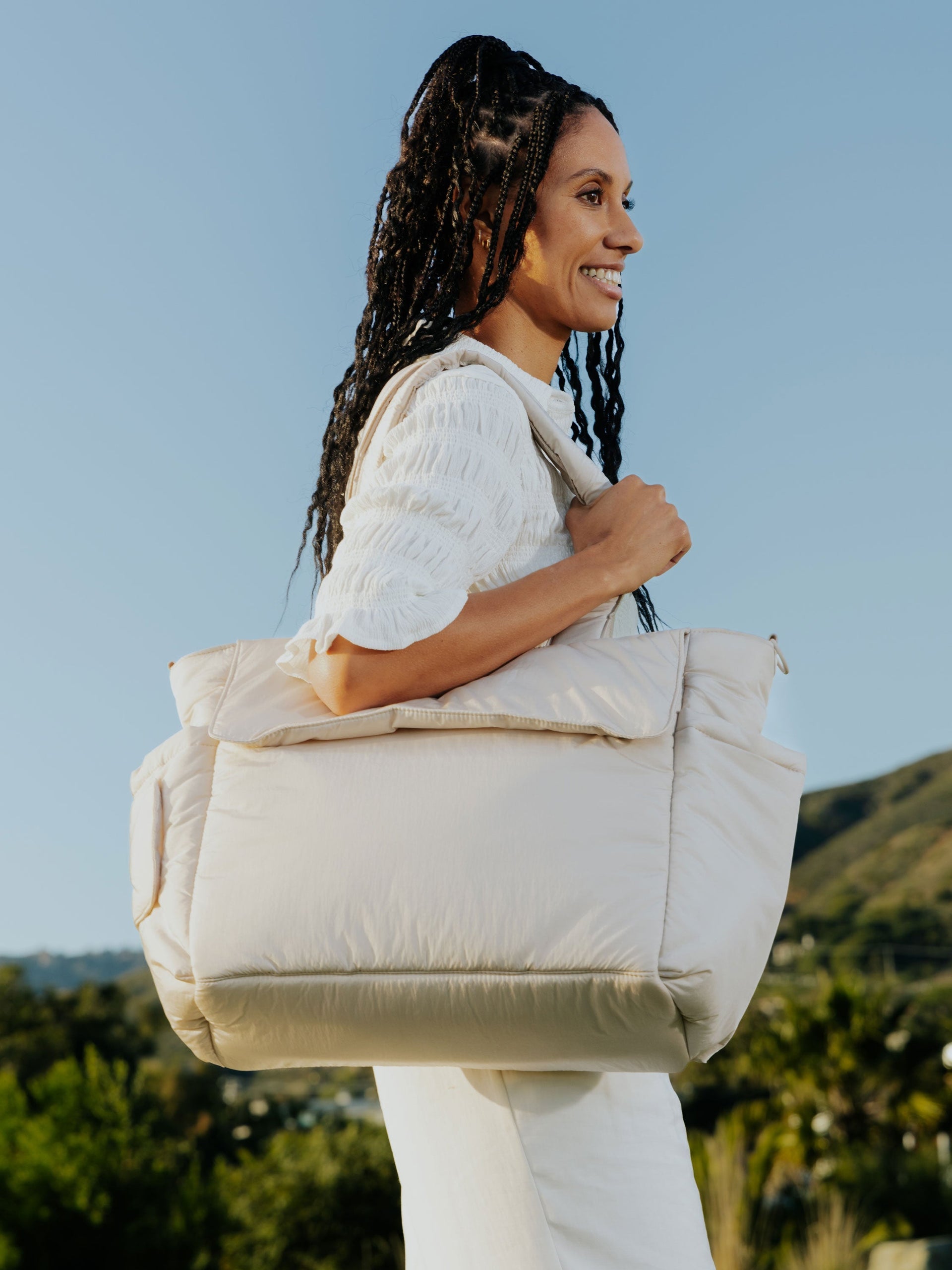 Model wearing CALPAK Diaper Tote Bag with Laptop Sleeve over shoulder in oatmeal; TBB2401-OATMEAL