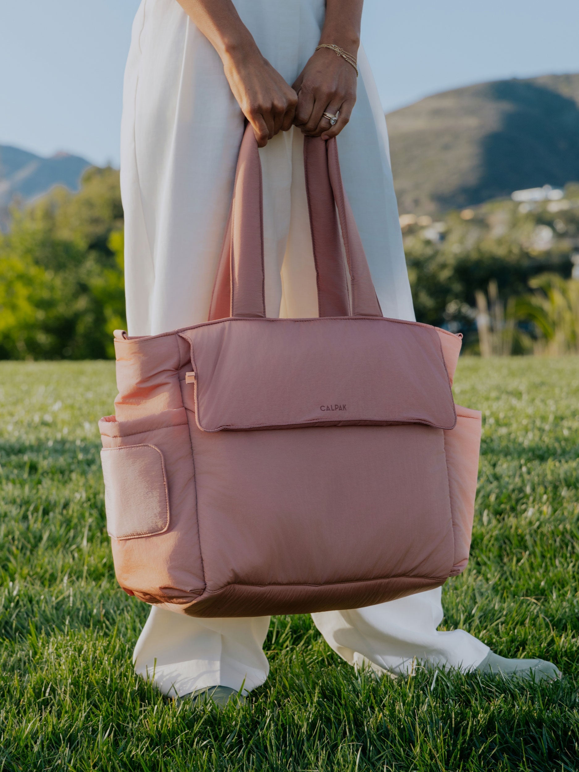 Model holding peony CALPAK Diaper Tote Bag with Laptop Sleeve by handles; TBB2401-PEONY
