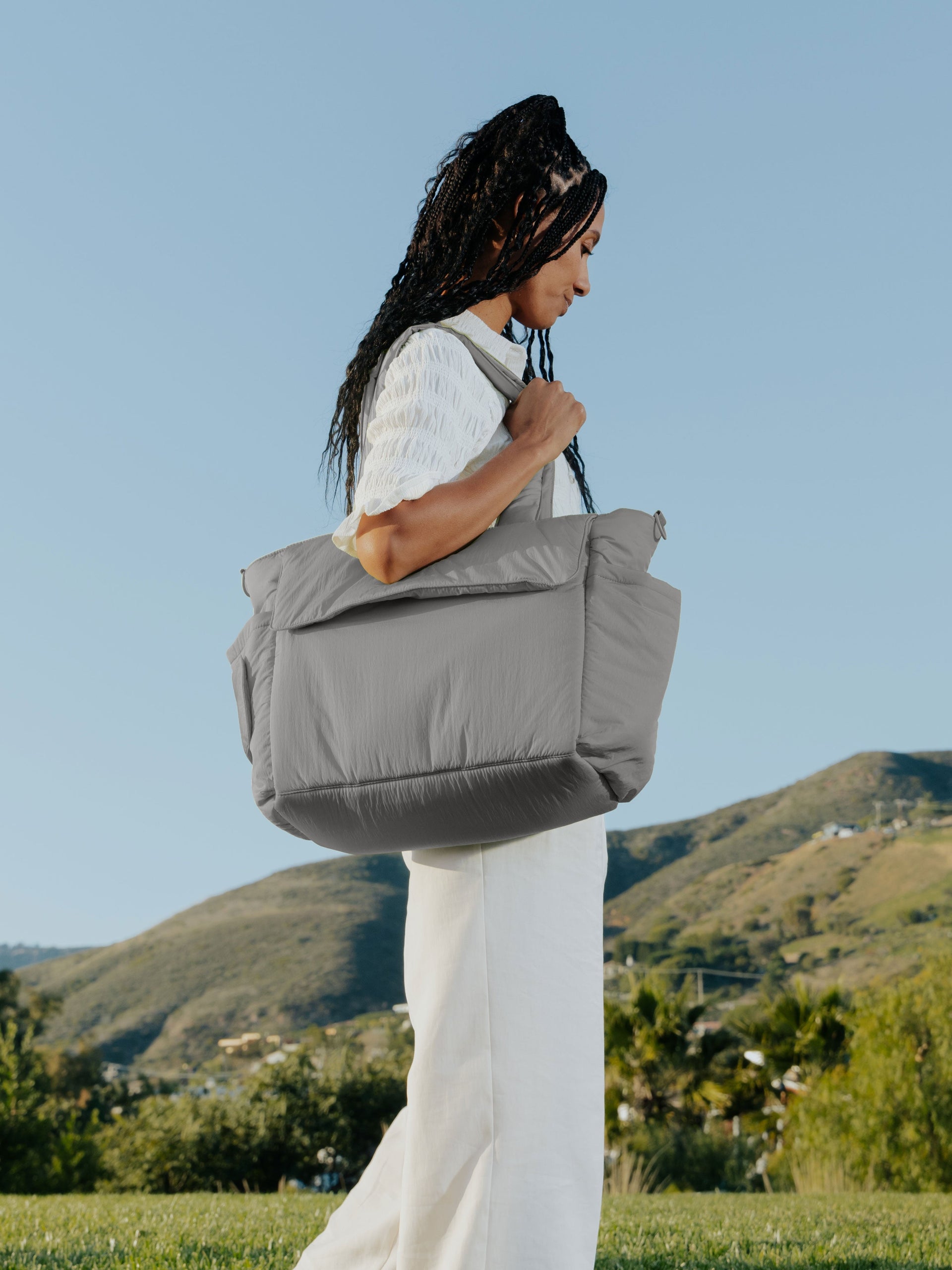 Model wearing slate gray CALPAK Diaper Tote Bag with Laptop Sleeve over shoulder; TBB2401-SLATE