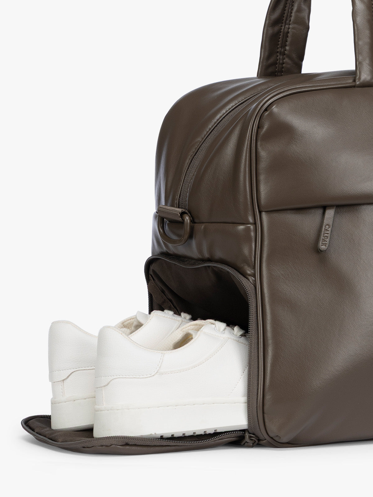 Side shoe compartment of A dark brown Mushroom CALPAK Luka Duffel in vegan leather with dual top handles and a front zippered pocket, photographed against a clean white background; DSM1901-MUSHROOM-PU