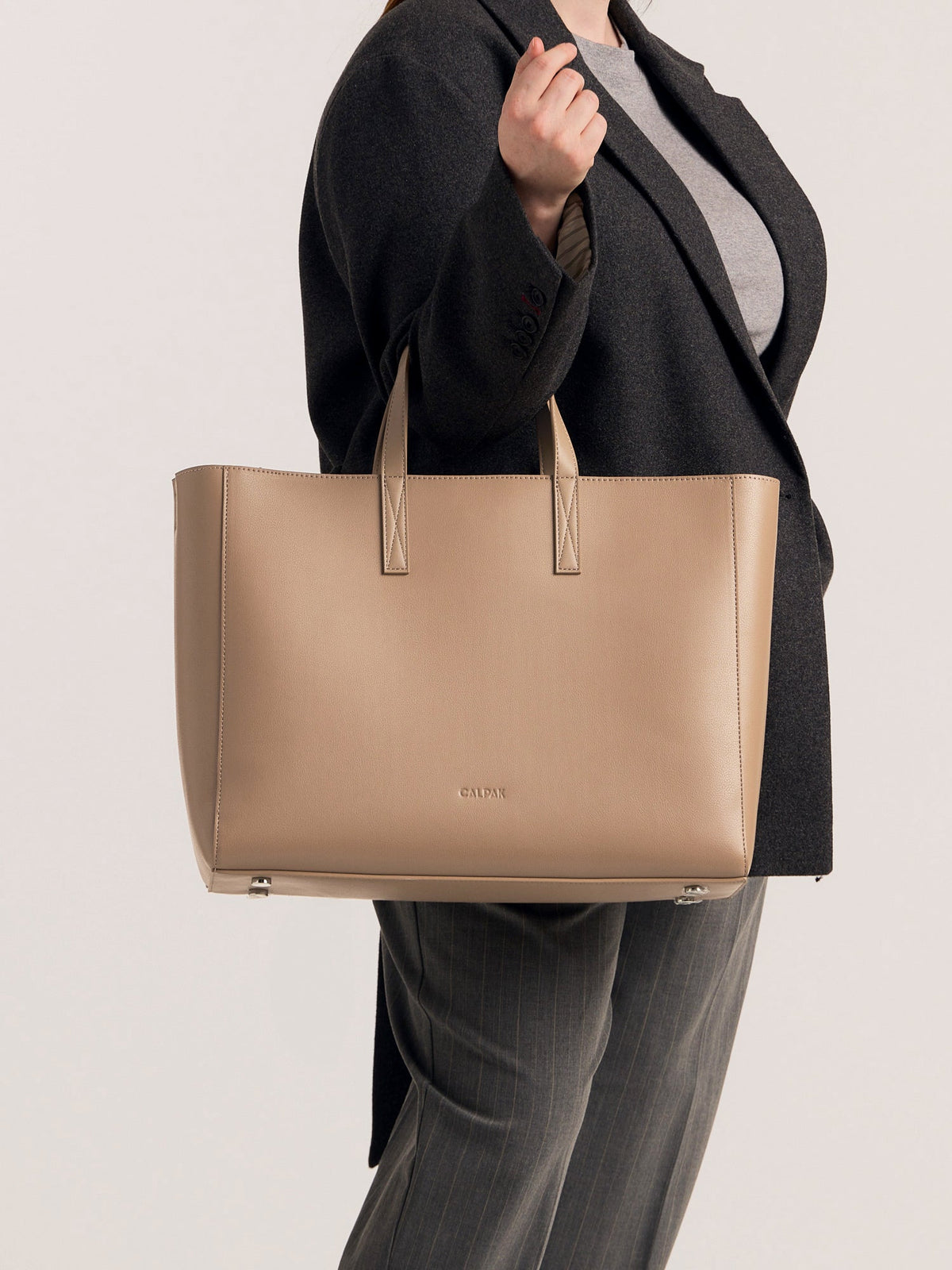 CALPAK Haven Laptop Tote Bag in light beige Taupe with model carrying it on forearm; ATO2102-TAUPE