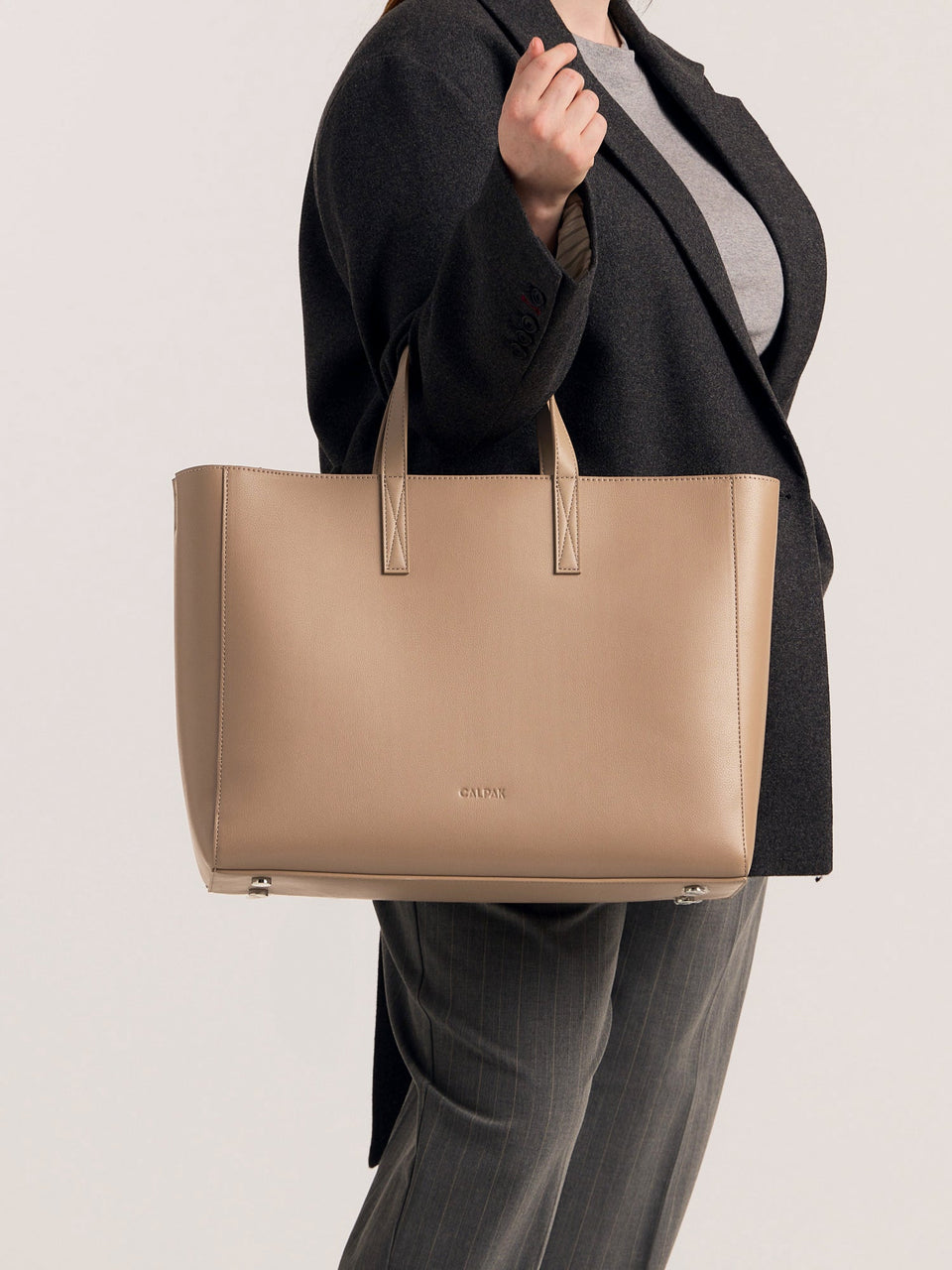 CALPAK Haven Laptop Tote Bag in light beige Taupe with model carrying it on forearm; ATO2102-TAUPE