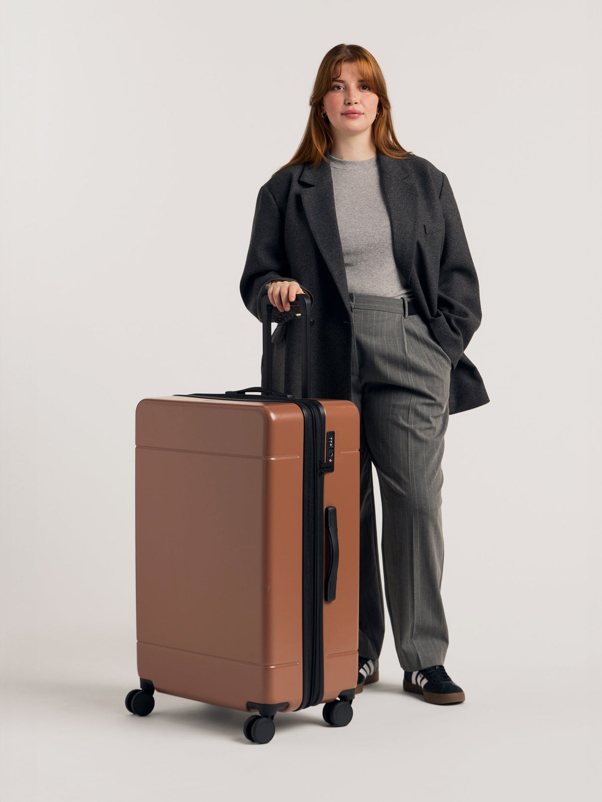 Model with CALPAK Hue large 30 inch hard shell luggage in brown Hazel color; LHU1028-HAZEL