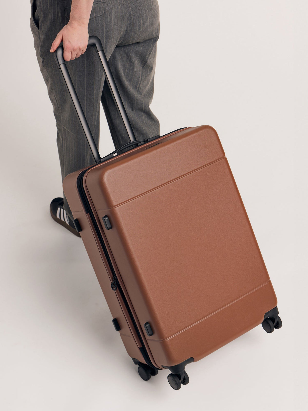 Model rolling with CALPAK Hue Medium Hardside Luggage in brown hazelnut; LHU1024-HAZEL 