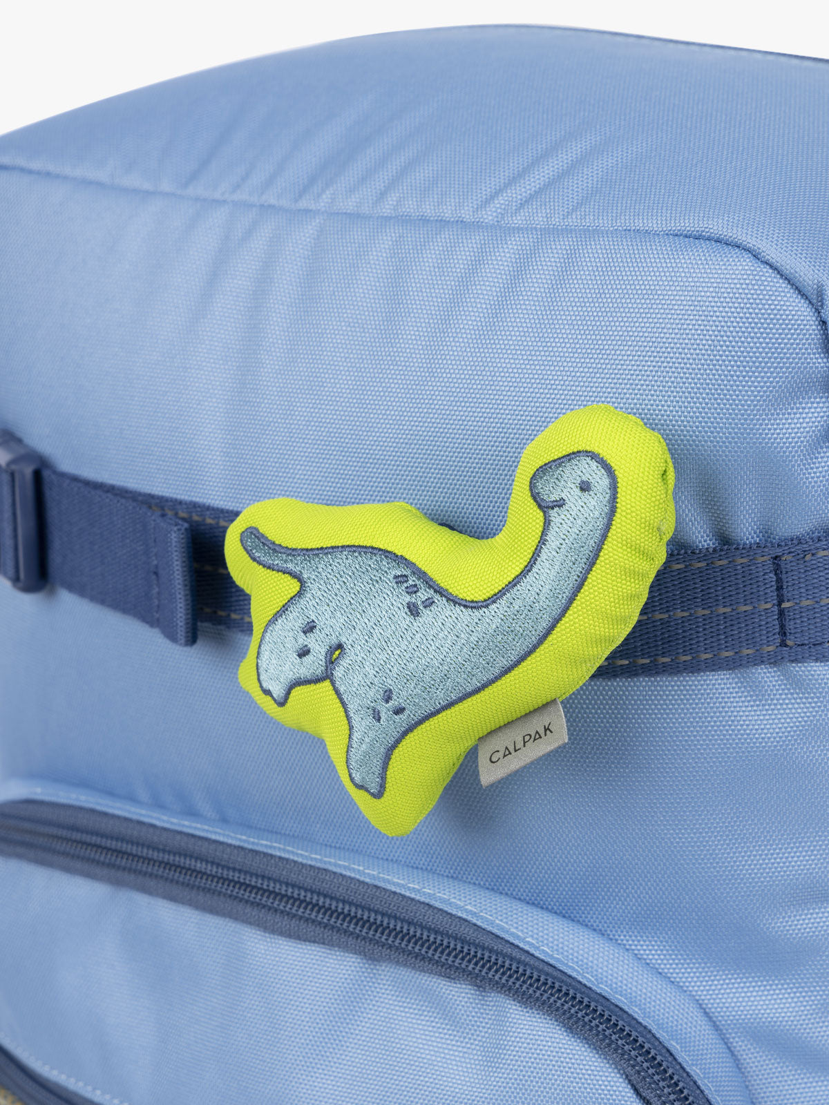 CALPAK Kids Collection blue and green Dinosaur Pluffy Bag Charm attached to Kids Large Blue Backpack; BCKL5000-BLUE