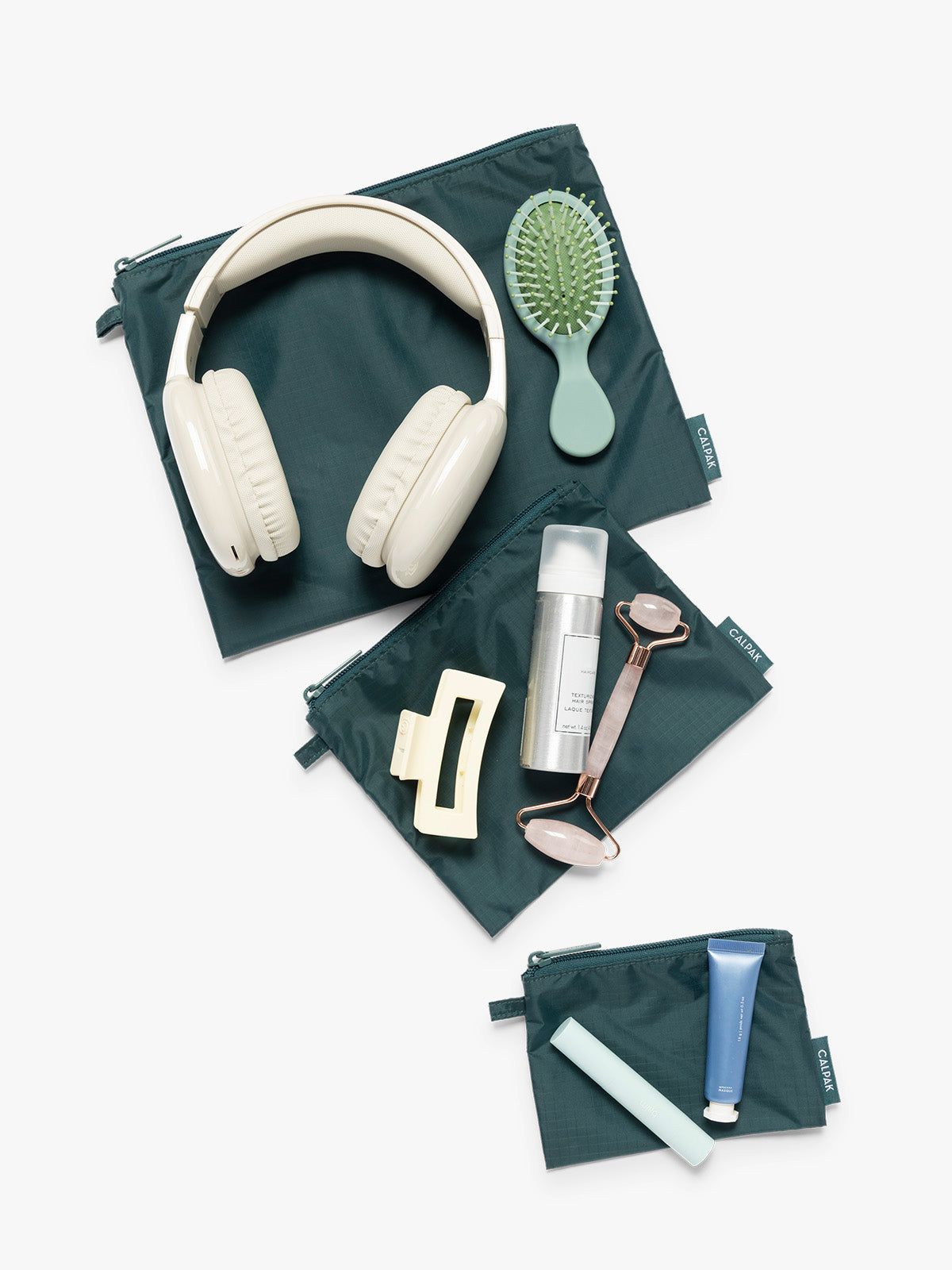Items on top of the three dark green teal Kale CALPAK Compakt Zippered pouches of different sizes, with items on top showing what fits inside, on a clean white background; KZB2001-KALE