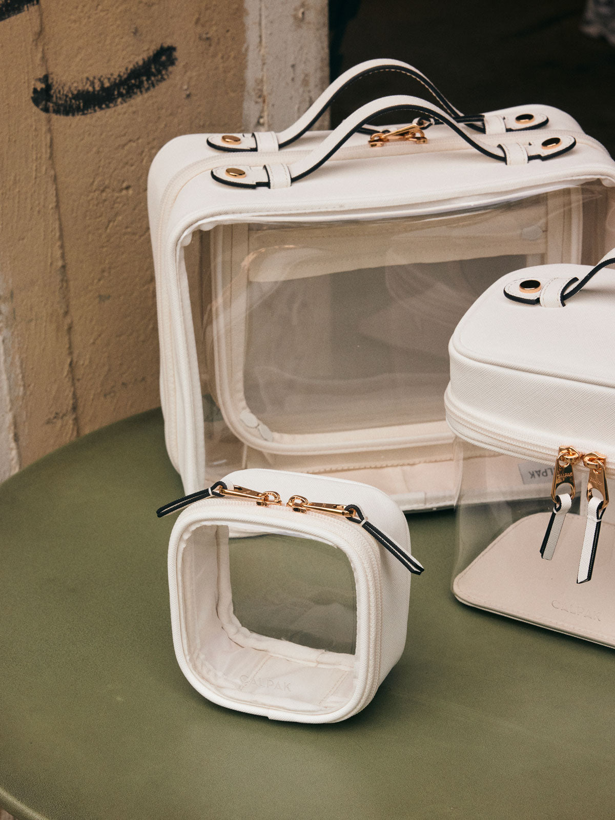 CALPAK Large Clear Cosmetics Case  on a green table with other CALPAK white Clear Cosmetic Cases; CCC2001-WHITE