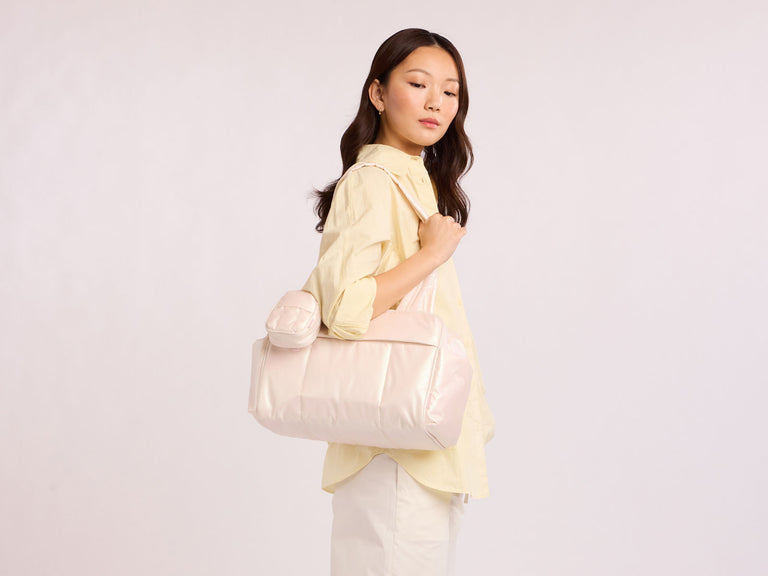 Woman holding a light pink CALPAK handbag against a plain background