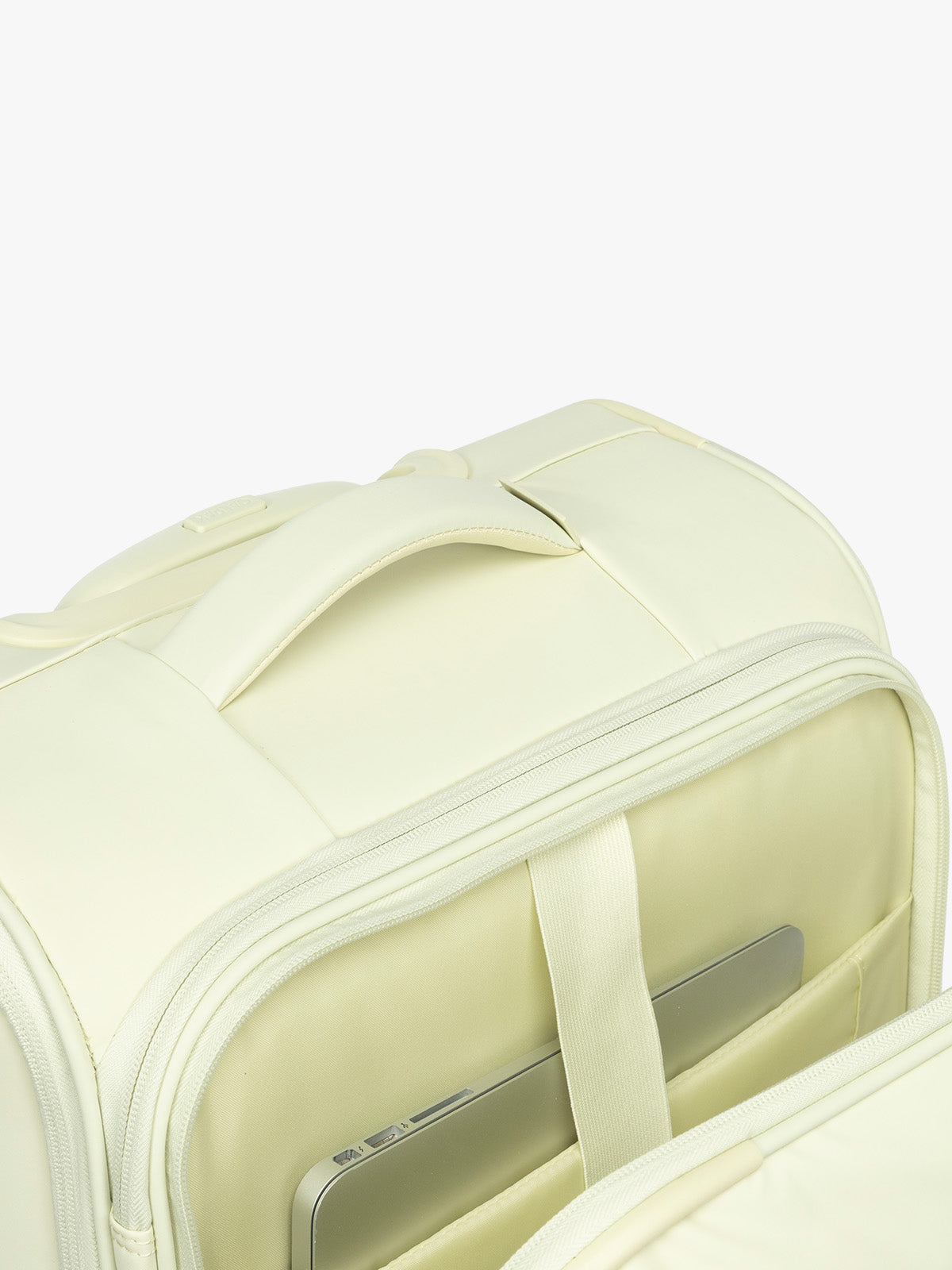 Top grab handle and front laptop sleeve of the CALPAK Luka Soft-Sided Carry On Luggage in light green Celadon on a white background with handle and spinner wheels; LSM1020-CELADON
