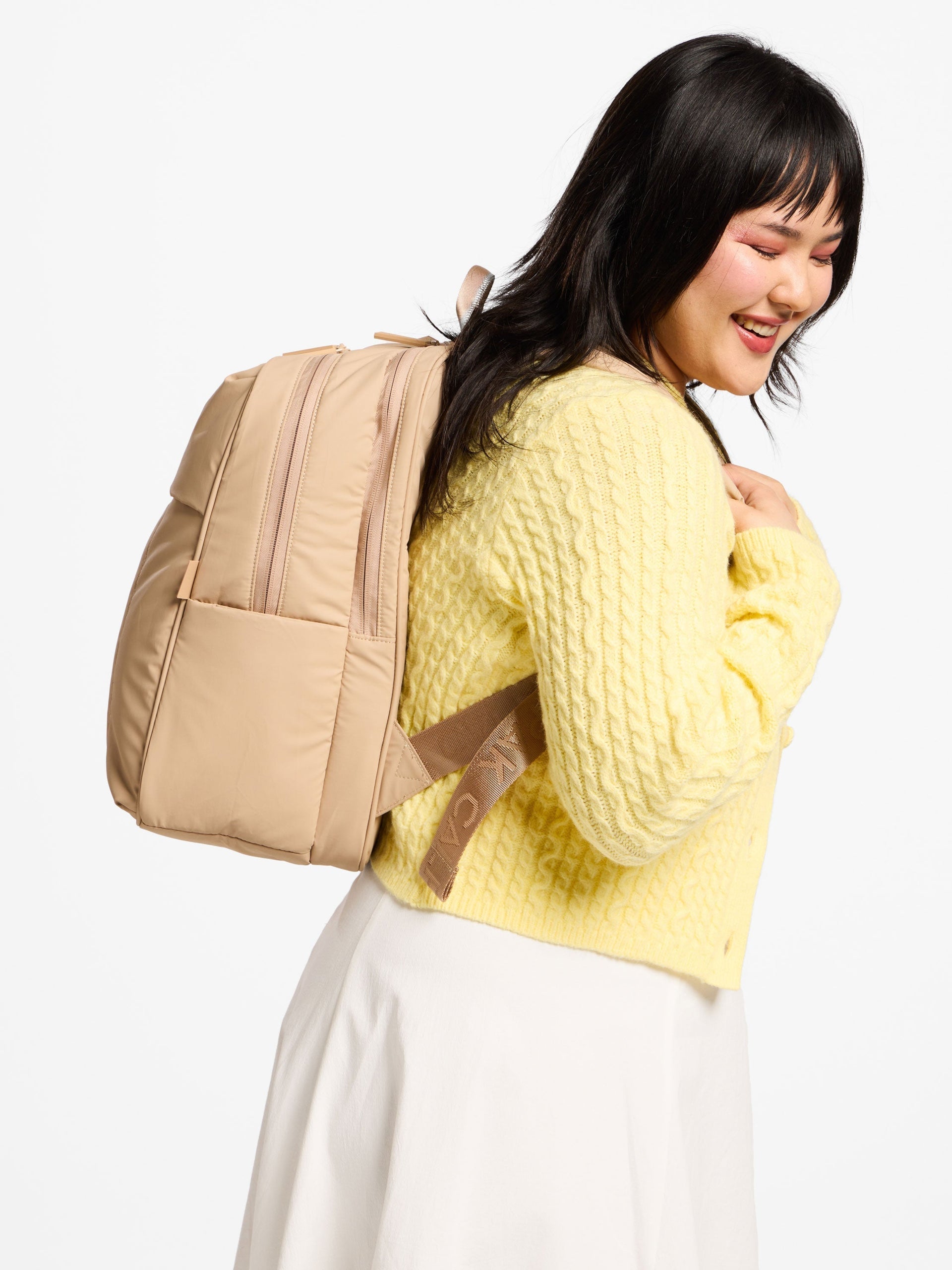 Model wearing latte puffy CALPAK laptop backpack for 15 inch laptop; BPL2001-LATTE