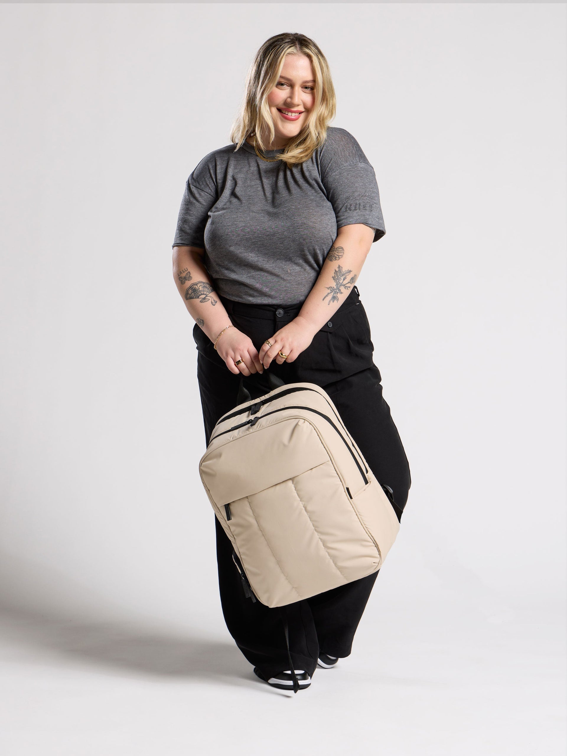Model holding CALPAK 17 inch Laptop Backpack in beige oatmeal; BPX2301-OATMEAL