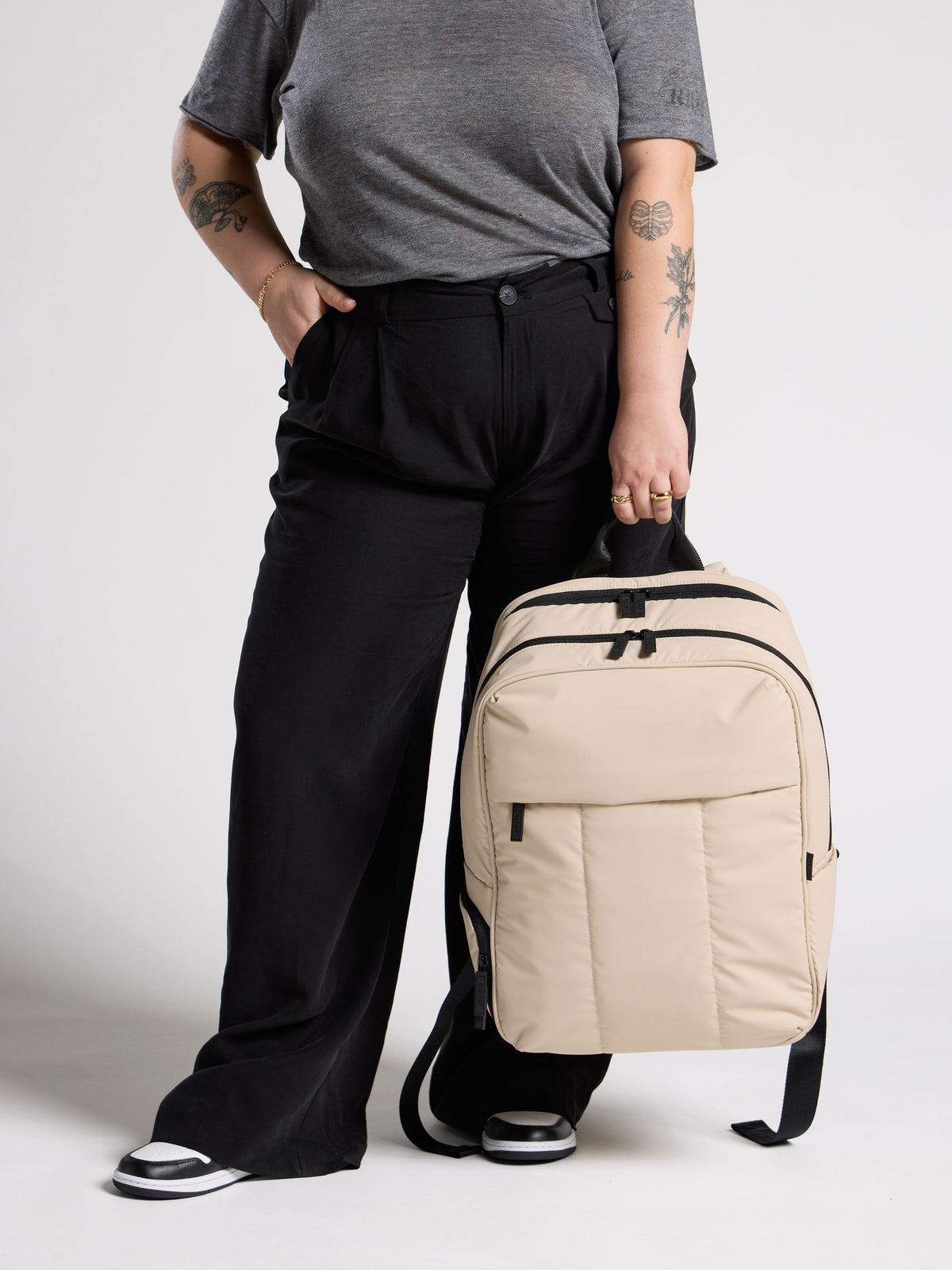 Model holding sofy, puffy CALPAK Luka 17 inch Laptop Backpack in oatmeal with water resistant exterior; BPX2301-OATMEAL