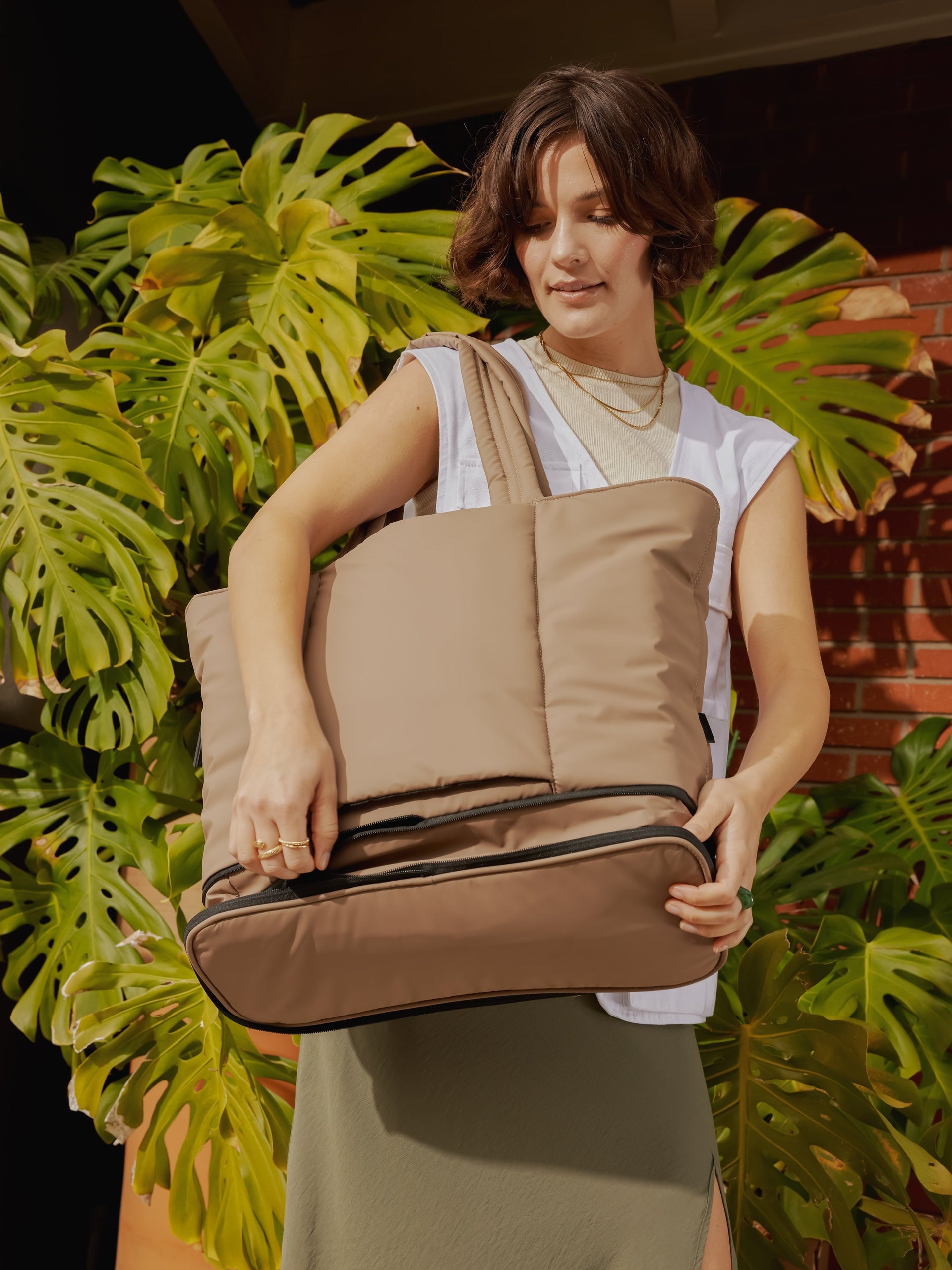 Model carrying CALPAK Luka expandable travel bag with laptop compartment in chocolate; ALT2201-CHOCOLATE
