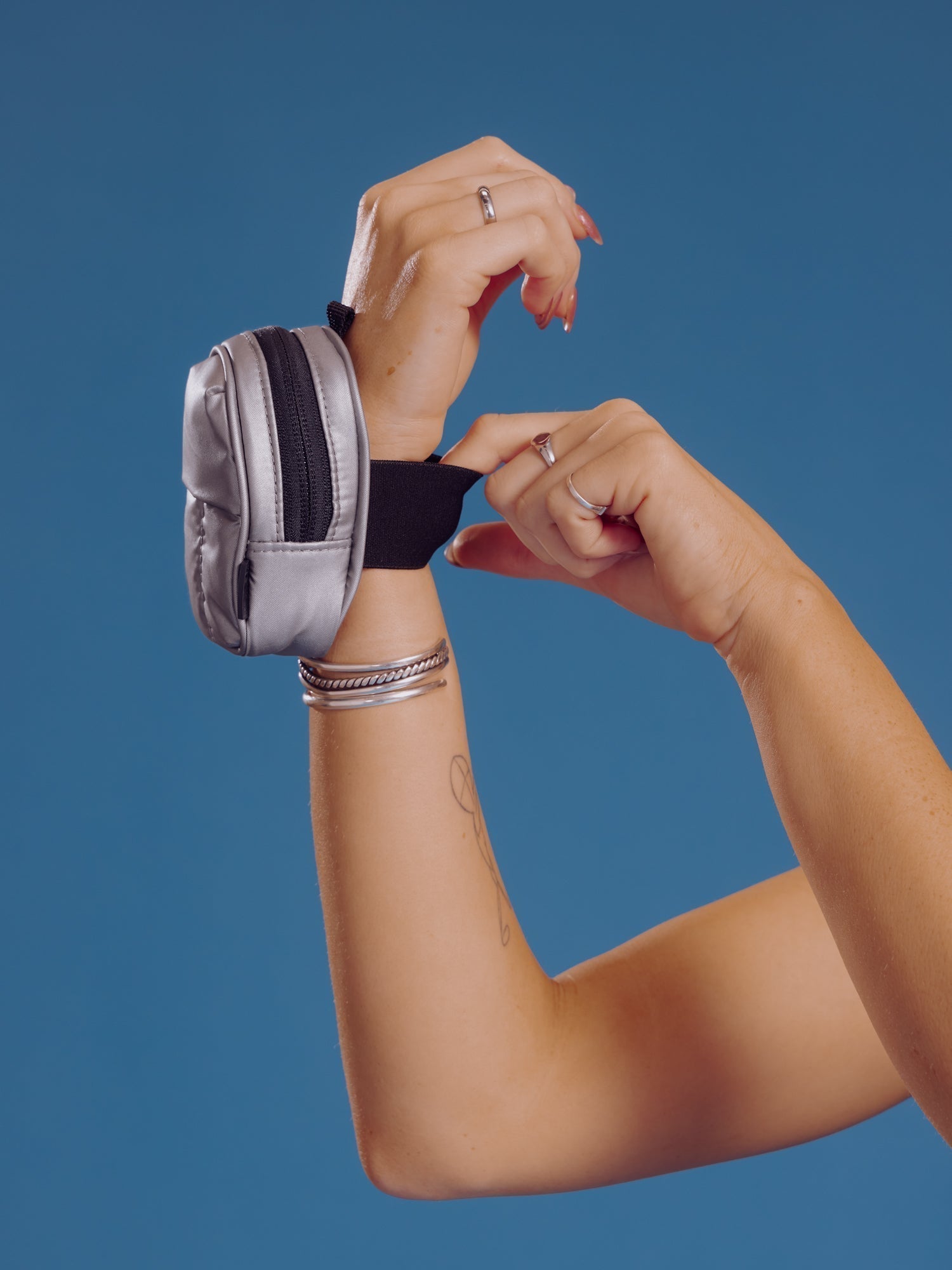 Model wearing gunmetal CALPAK Luka Key Pouch around wrist and displaying elastic wristband; AMB2201-GUNMETAL