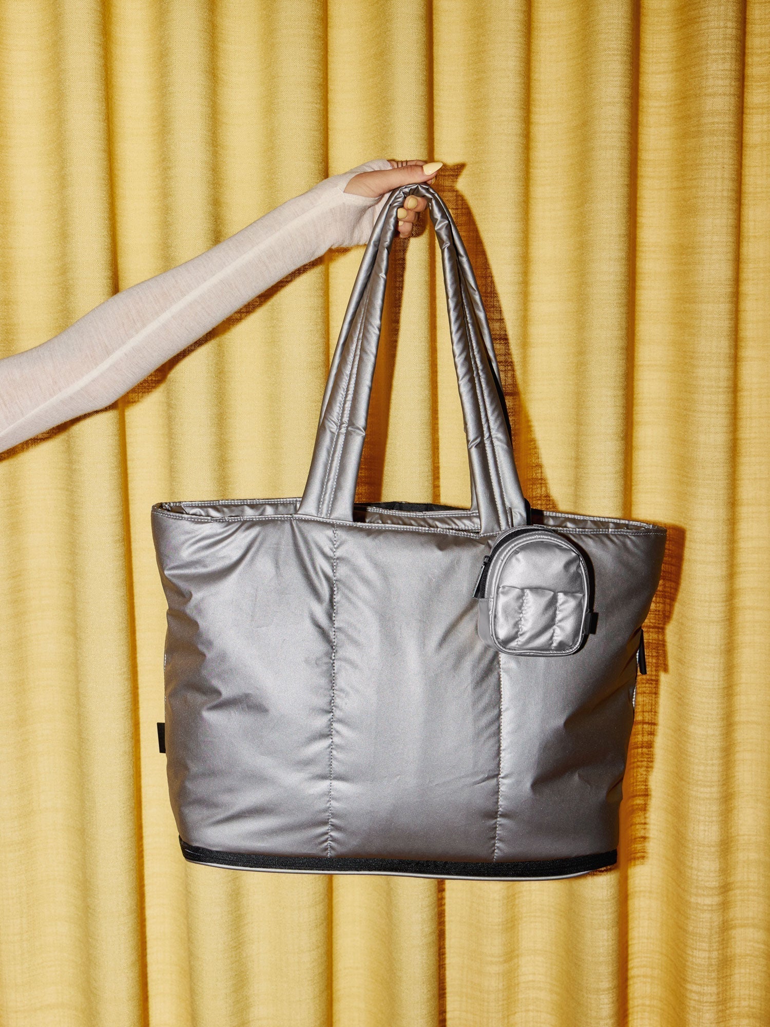 Model holding up CALPAK Luka Expandable Laptop Tote with Luka Key Pouch clipped to strap in metallic silver; AMB2201-GUNMETAL