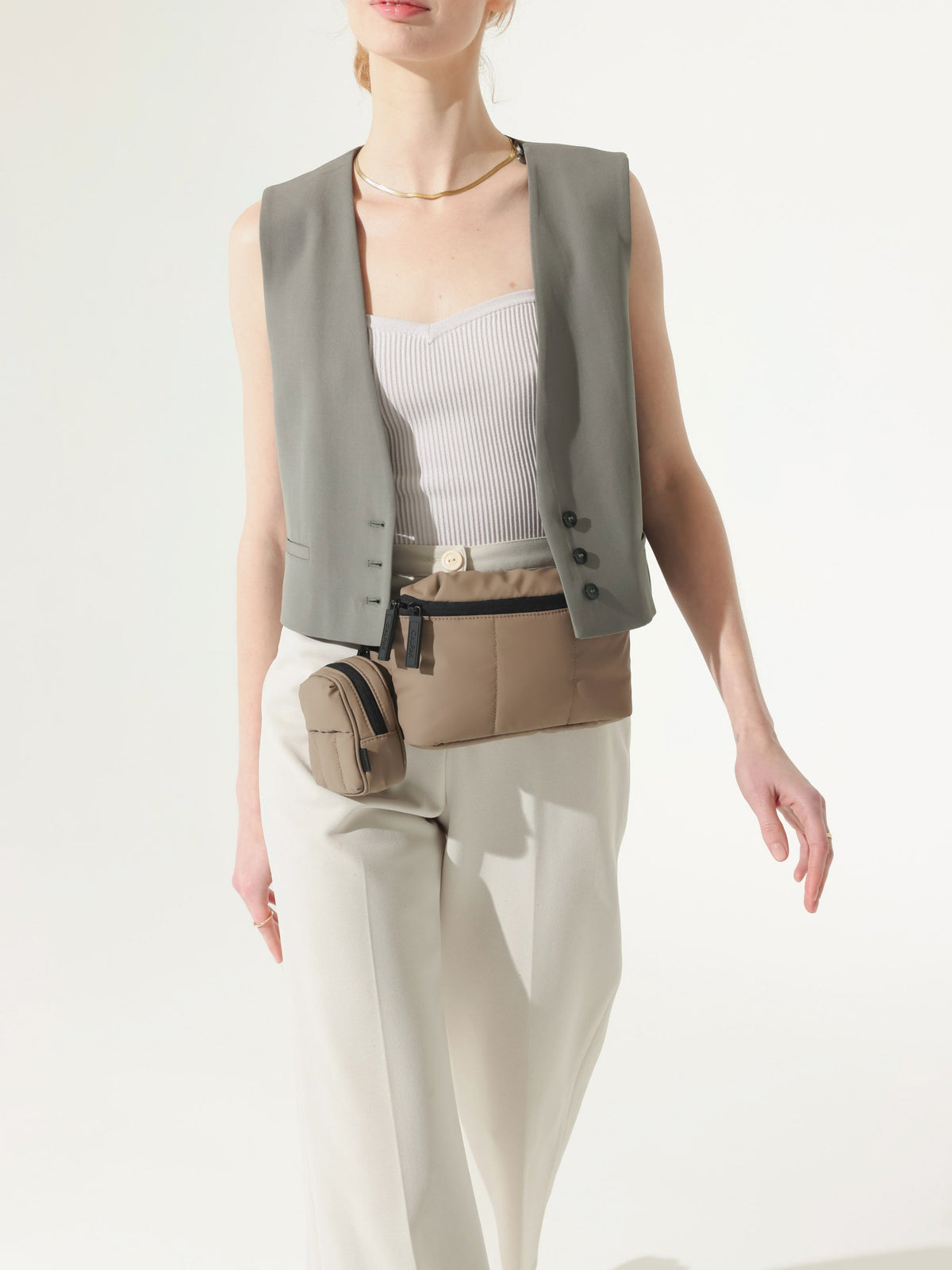 Model wearing CALPAK Luka coin purse keychain attached to fanny pack in brown;   AMB2201-CHOCOLATE