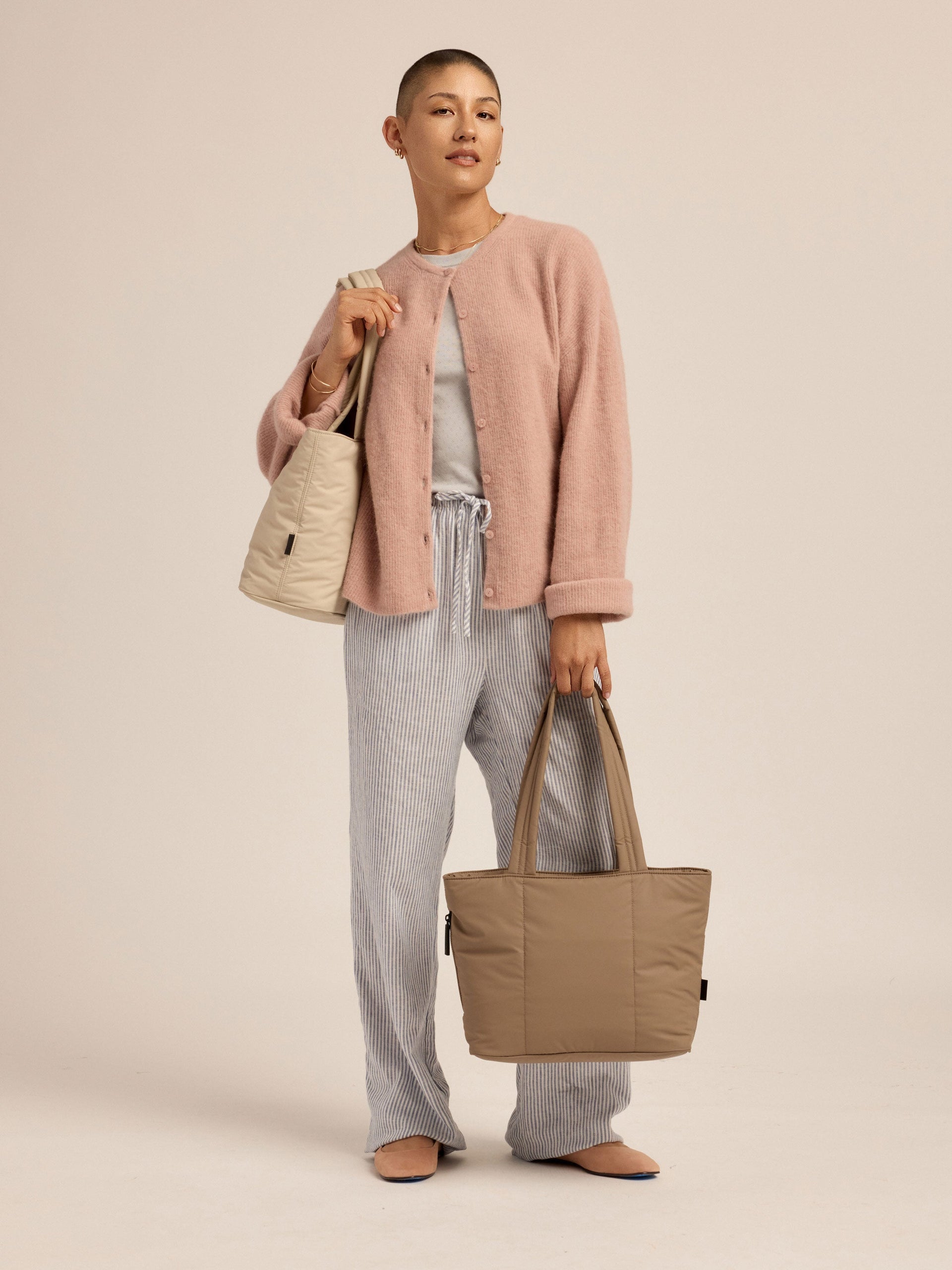 Model wearing oatmeal CALPAK Luka Mini Tote over shoulder with the chocolate Luka Mini Tote in the other hand; ALM2401-CHOCOLATE