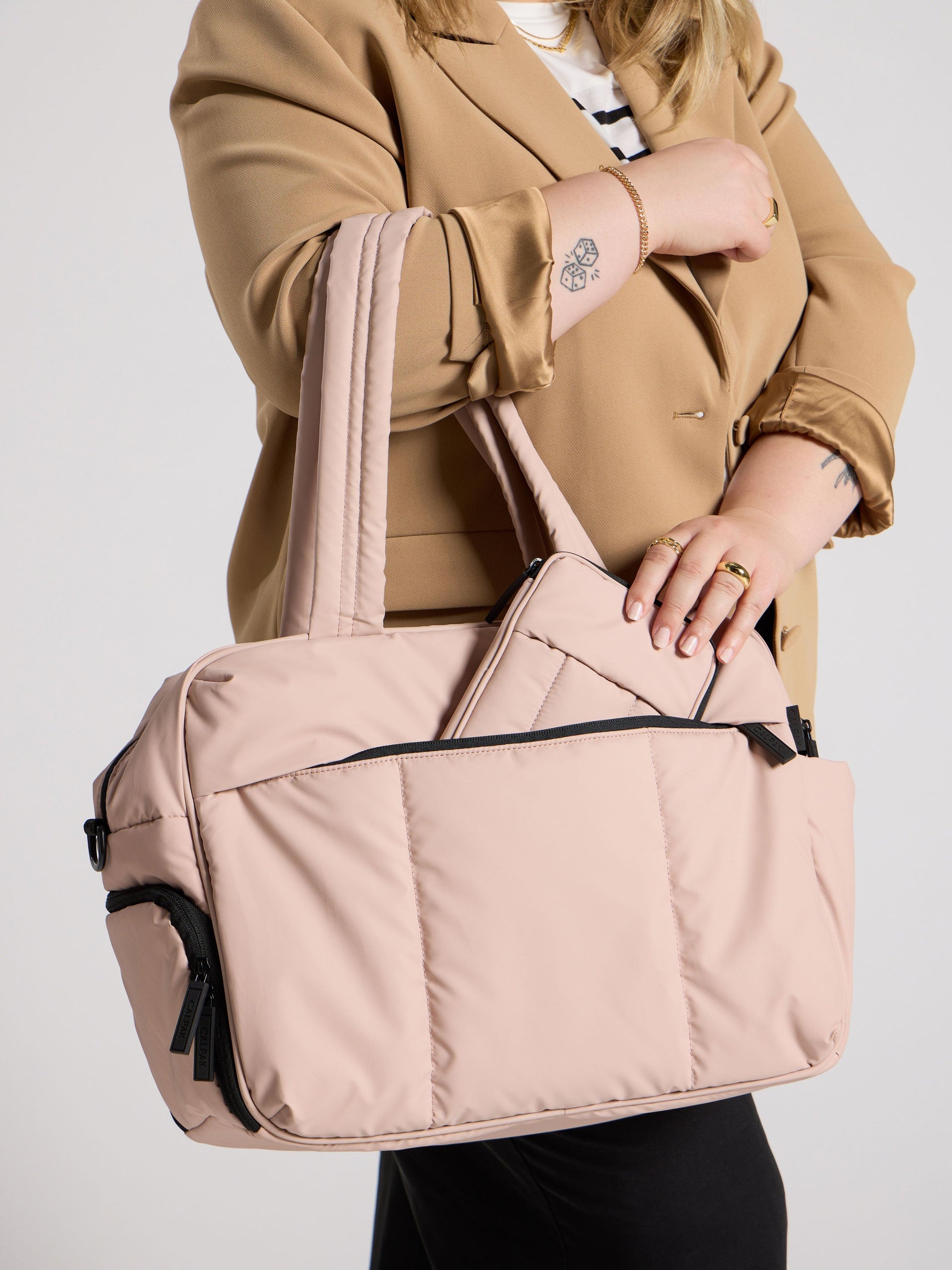 Model placing rose quartz CALPAK Luka Zippered Passport Wallet inside front pocket of Luka Duffel in rose quartz; PZW2301-ROSE-QUARTZ