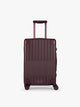 CALPAK Vault deep red Dark Cherry hard-shell spinner Carry On Luggage with a telescoping handle extended, featuring a deep red leatherette side handle and trim, set against a plain light gray background; LVT1020-DARK-CHERRY