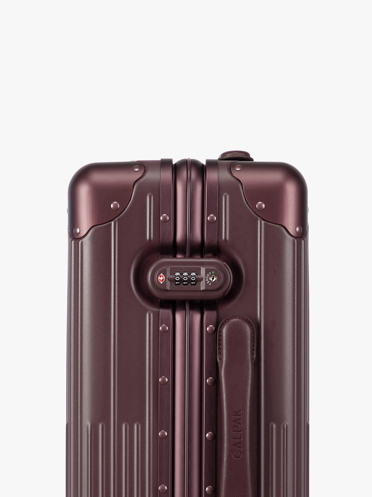 Closeup of the TSA-approved lock of CALPAK Vault deep red Dark Cherry hard-shell spinner Carry On Luggage with a telescoping handle extended, featuring a deep red leatherette side handle and trim, set against a plain light gray background; LVT1020-DARK-CHERRY
