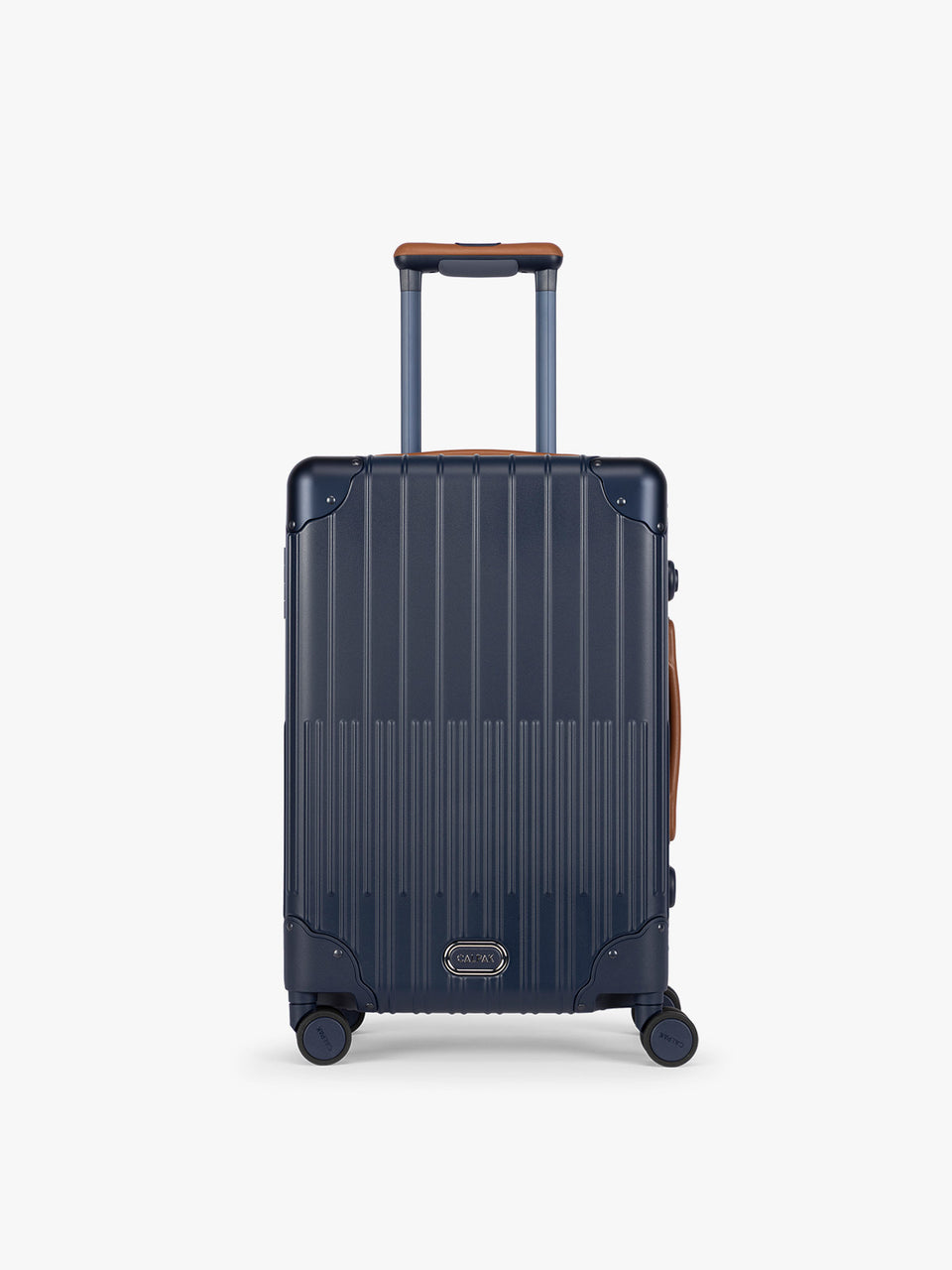 CALPAK Vault Navy blue hard-shell spinner Carry On Luggage with a telescoping handle extended, featuring a brown leatherette side handle and trim, set against a plain light gray background; LVT1020-NAVY
