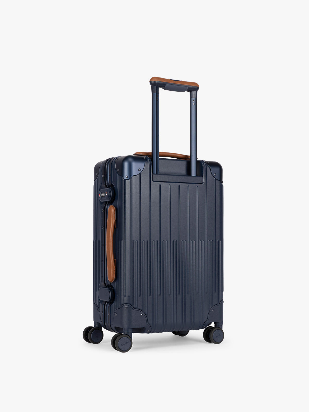 Backside of CALPAK Vault Navy blue hard-shell spinner Carry On Luggage with a telescoping handle extended, featuring a brown leatherette side handle and trim, set against a plain light gray background; LVT1020-NAVY