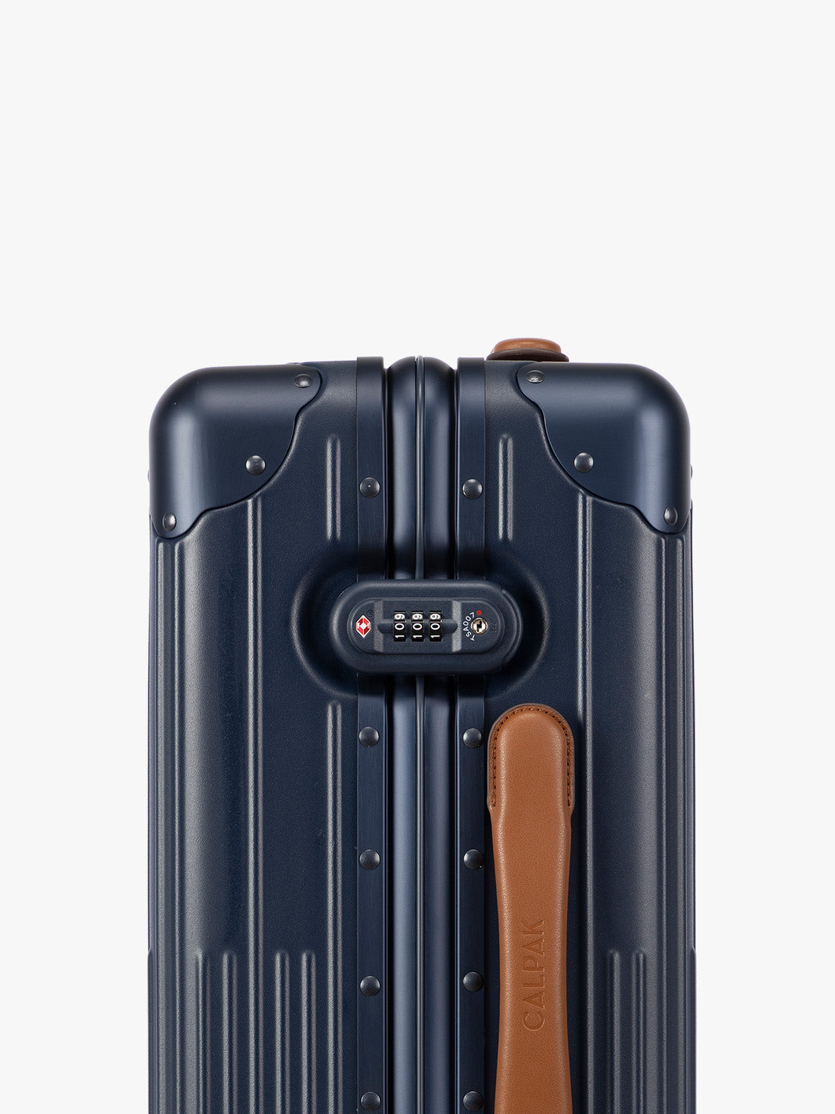 Closeup of side TSA lock of CALPAK Vault Navy blue hard-shell spinner Carry On Luggage with a telescoping handle extended, featuring a brown leatherette side handle and trim, set against a plain light gray background; LVT1020-NAVY