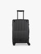 CALPAK Vault black Onyx hard-shell spinner Carry On Luggage with a telescoping handle extended, featuring a Black leatherette side handle and trim, set against a plain light gray background; LVT1020-ONYX